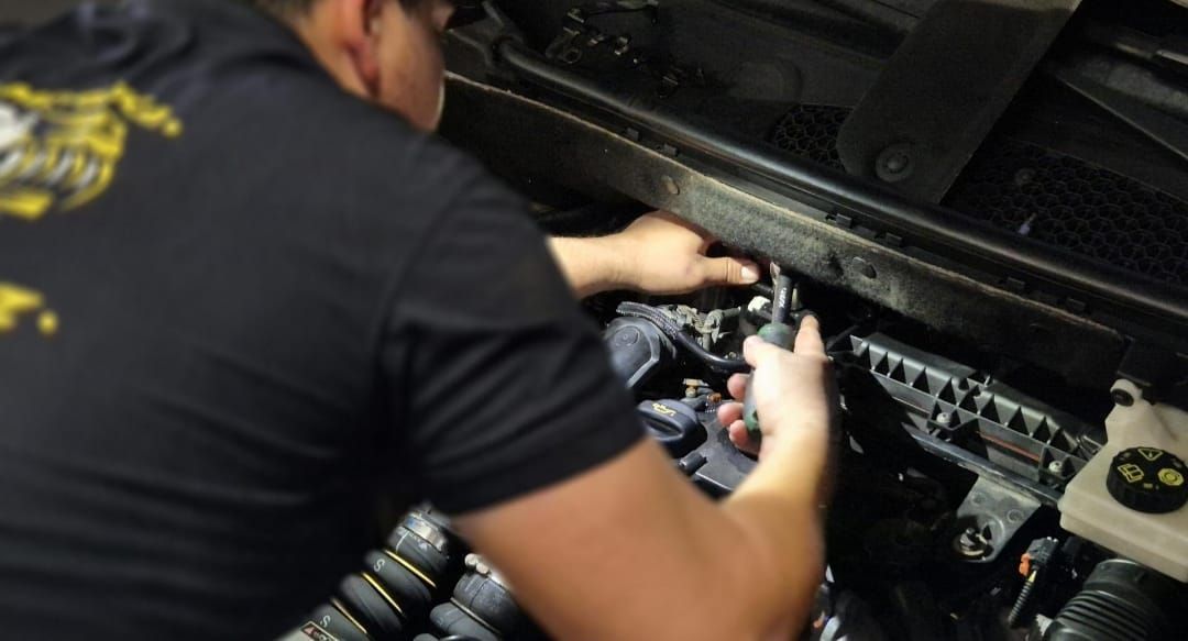 Mecánico trabajando en el motor de un coche, usando herramientas para realizar una reparación.