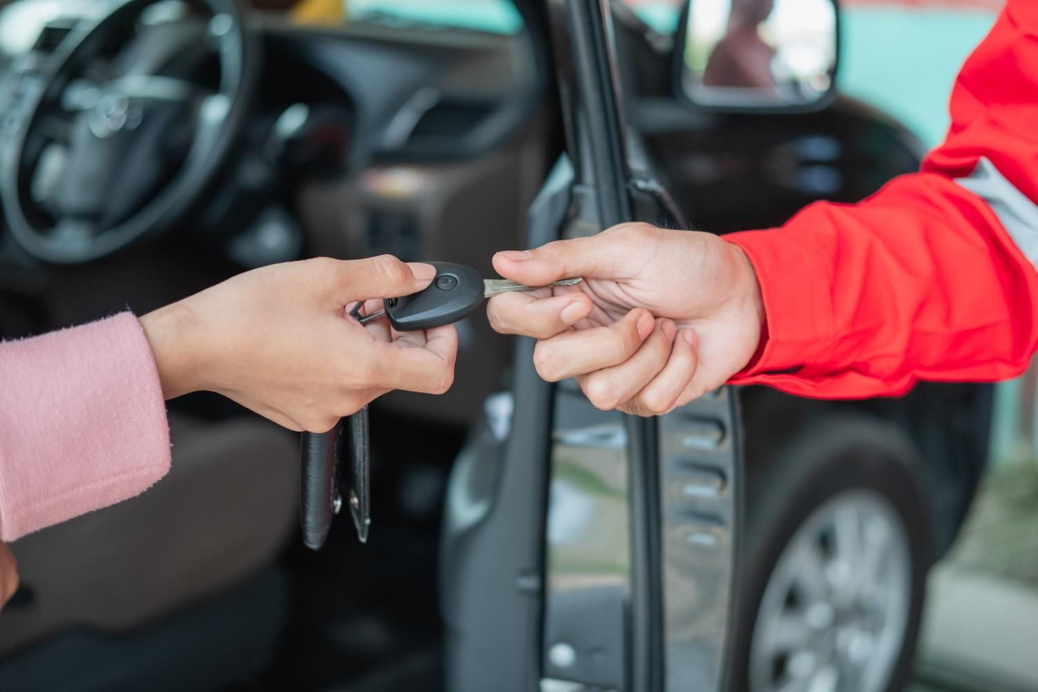 Persona entregando las llaves del coche a otra persona, cerca de la puerta del coche abierta.