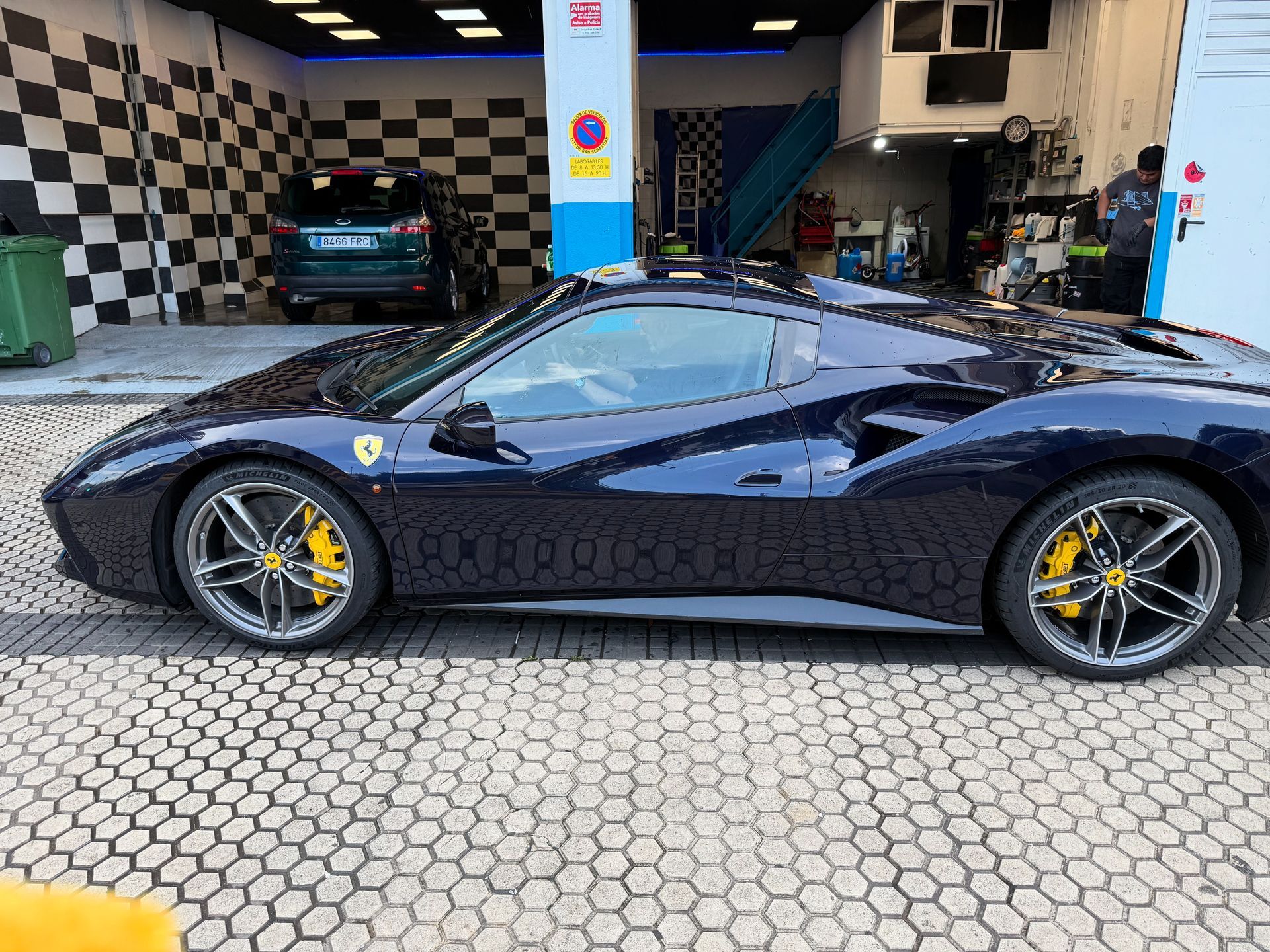 Coche deportivo Ferrari azul con pinzas de freno amarillas aparcado en un lavadero de coches.