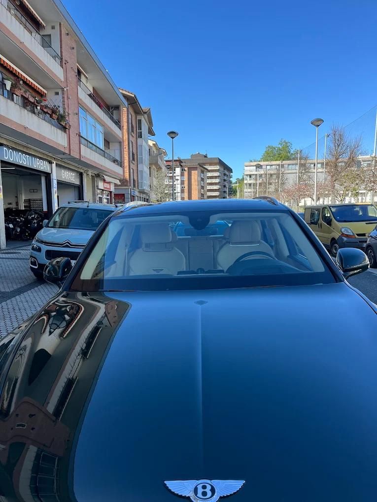 Coche Bentley verde oscuro aparcado en una calle con edificios, cielo despejado.
