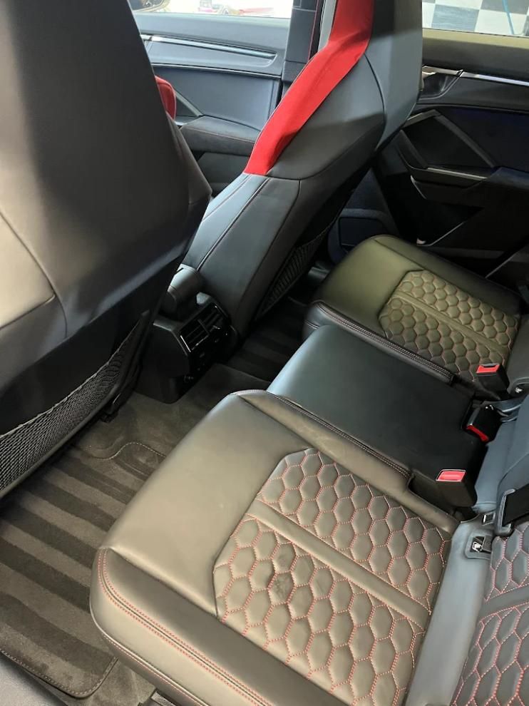 Interior negro y rojo con asientos acolchados. Asientos traseros visibles con reposacabezas y cinturones de seguridad.