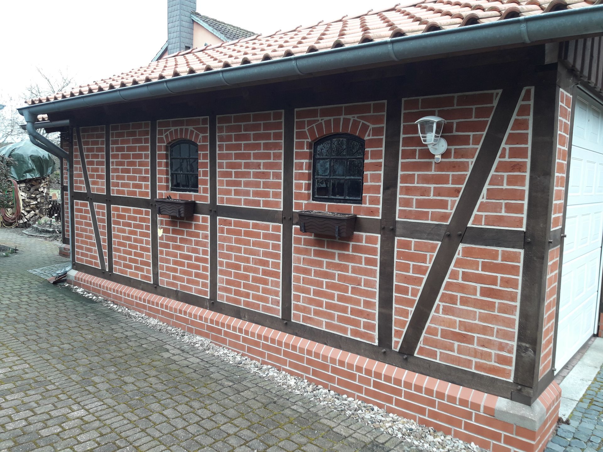 Ein Backsteingebäude mit Ziegeldach, Holzbalken, kleinen Fenstern und einer Leuchte an einem Kopfsteinpflasterweg.