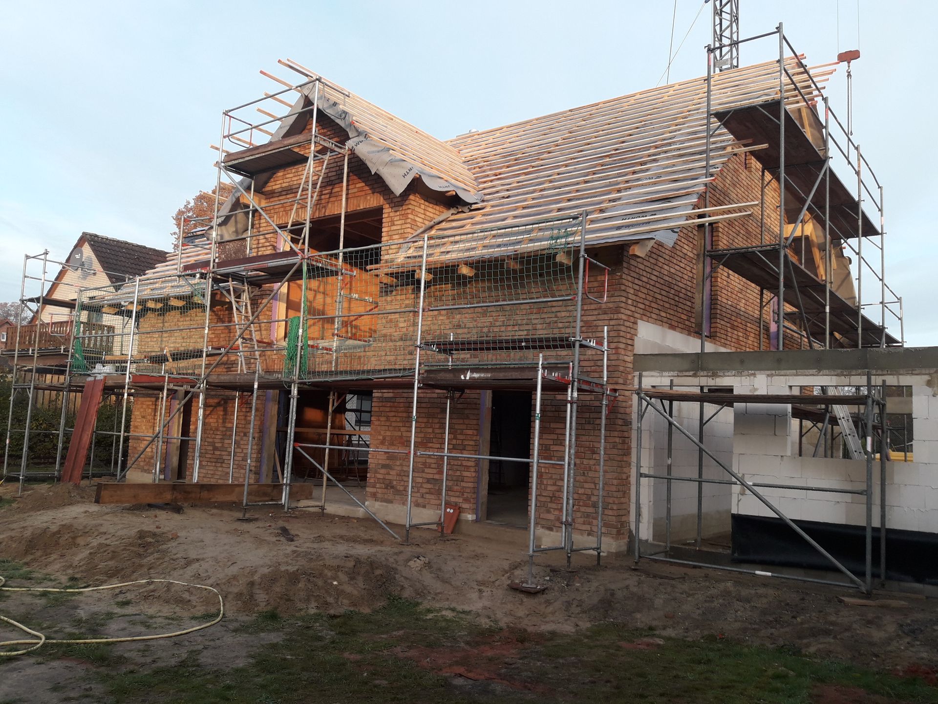 Ein teilweise eingerüstetes Backsteinhaus mit Schrägdach und offenem Innenraum umgeben von Baumaterialien.