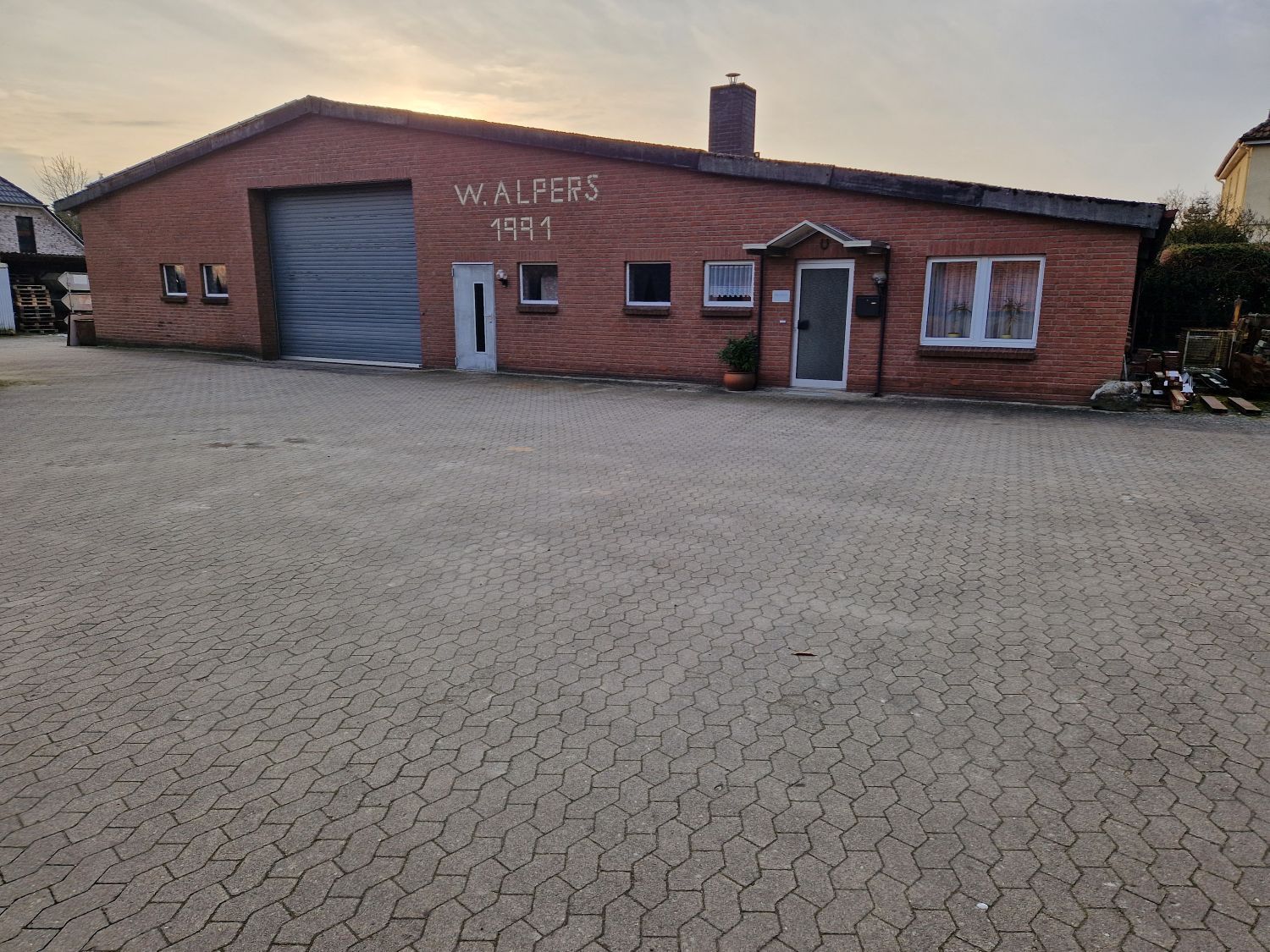 Ein rotes Backsteingebäude mit einem großen Garagentor und der Aufschrift „W. ALPERS 1991“ auf der Vorderseite.