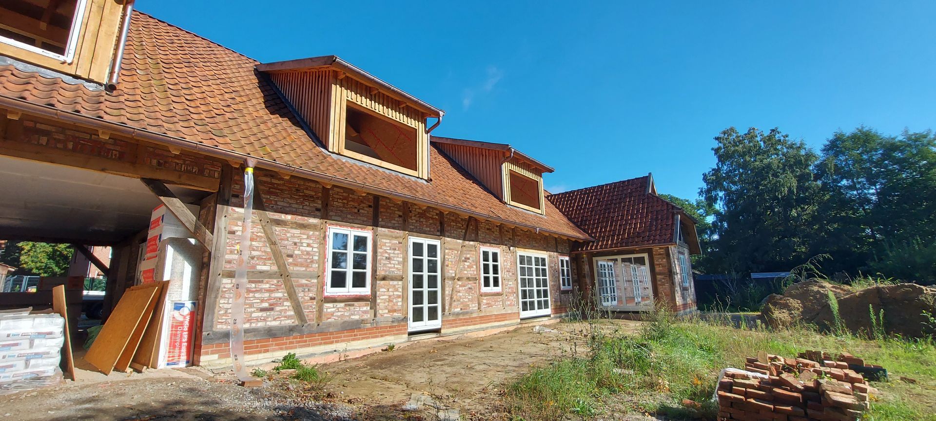Ein neu errichtetes Haus im rustikalen Stil mit Ziegeldach, Holzbalken und großen Fenstern.