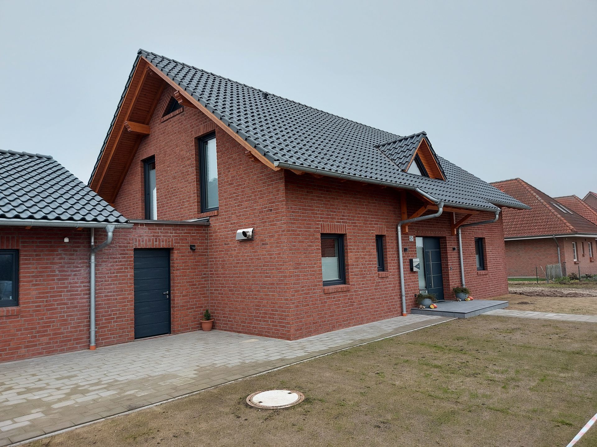 Ein modernes Backsteinhaus mit einem grauen Ziegeldach, einer schwarzen Tür.