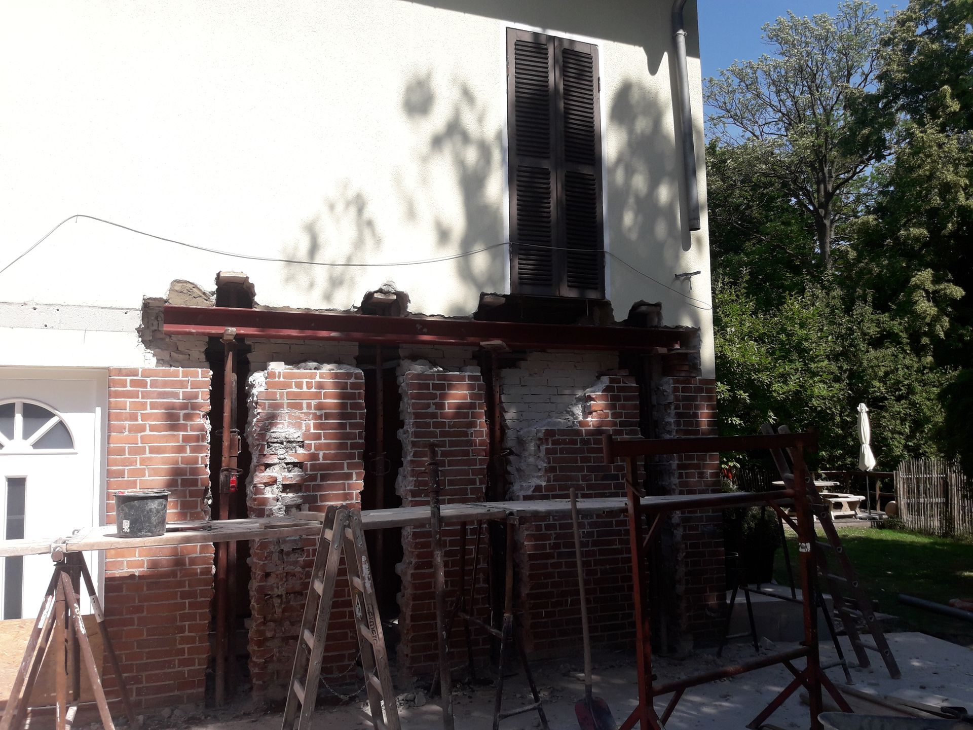 Eine teilweise abgerissene Ziegelmauer mit Stützbalken, Werkzeugen und Gerüsten.