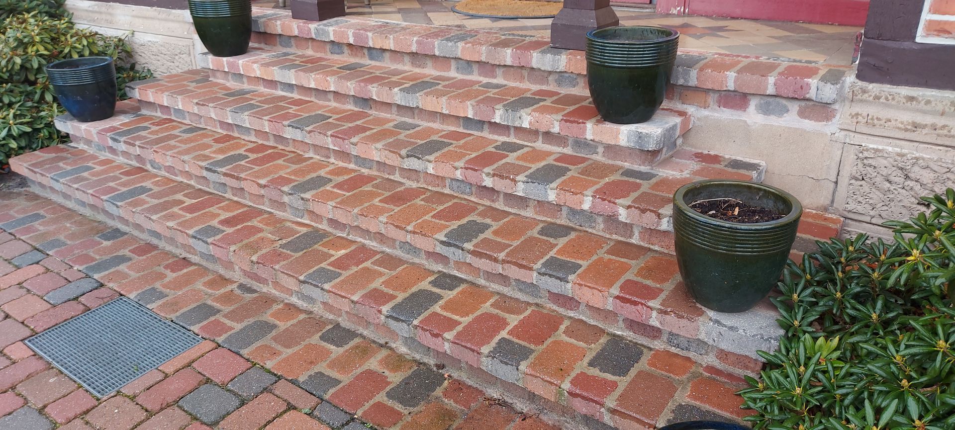 Eine Backsteintreppe mit fünf Stufen, flankiert von grünen Topfpflanzen.