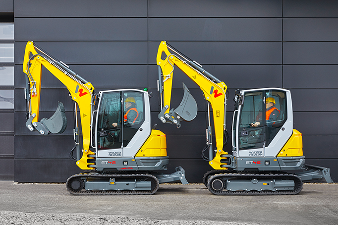 Dos excavadoras amarillas están estacionadas una al lado de la otra frente a un edificio.