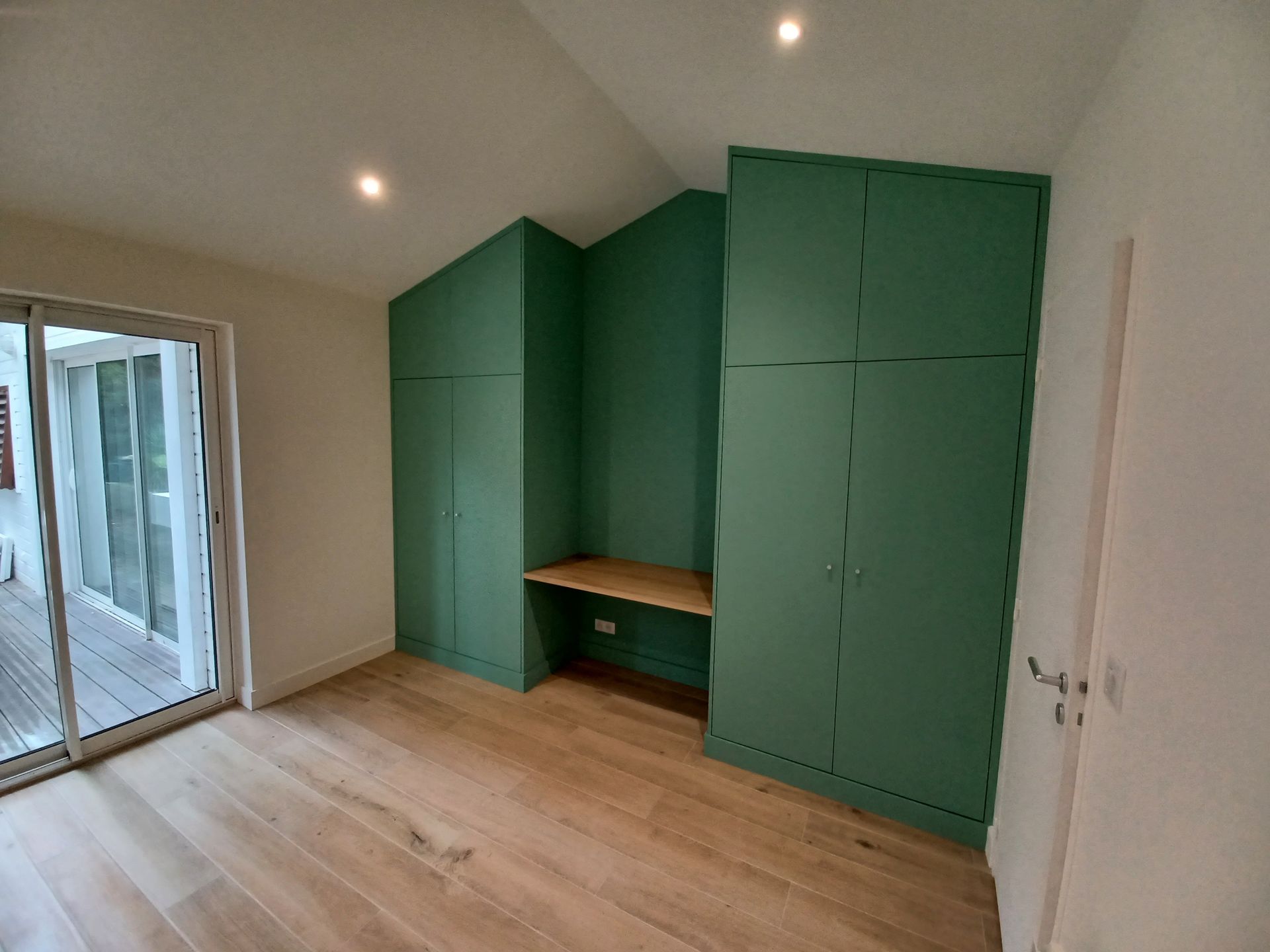 Armoires encastrées vertes avec bureau dans une pièce avec parquet en bois clair et porte coulissante en verre.
