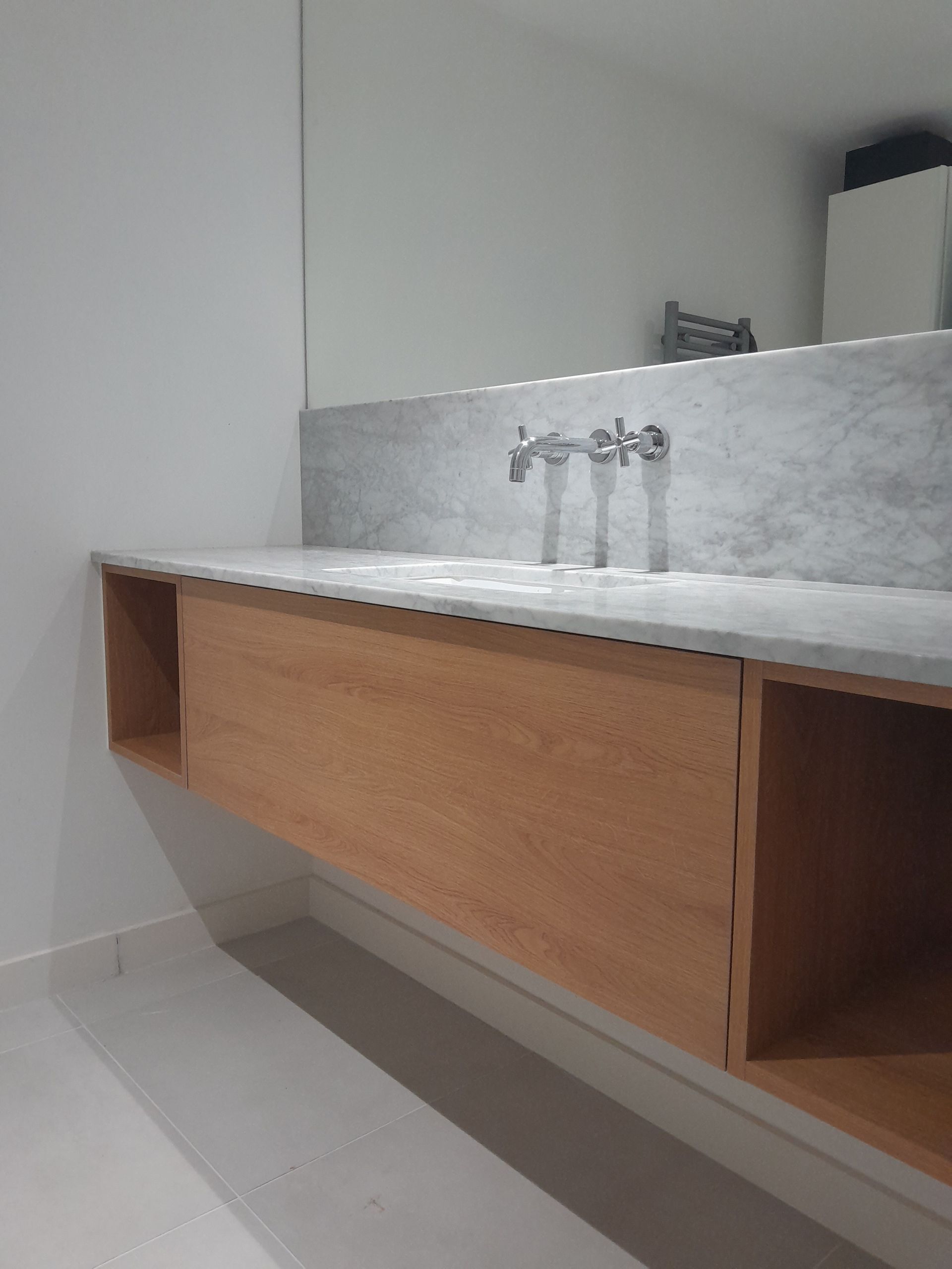 Meuble-lavabo avec flottant en bois, comptoir en marbre et robinet, sous un miroir dans une salle de bains.