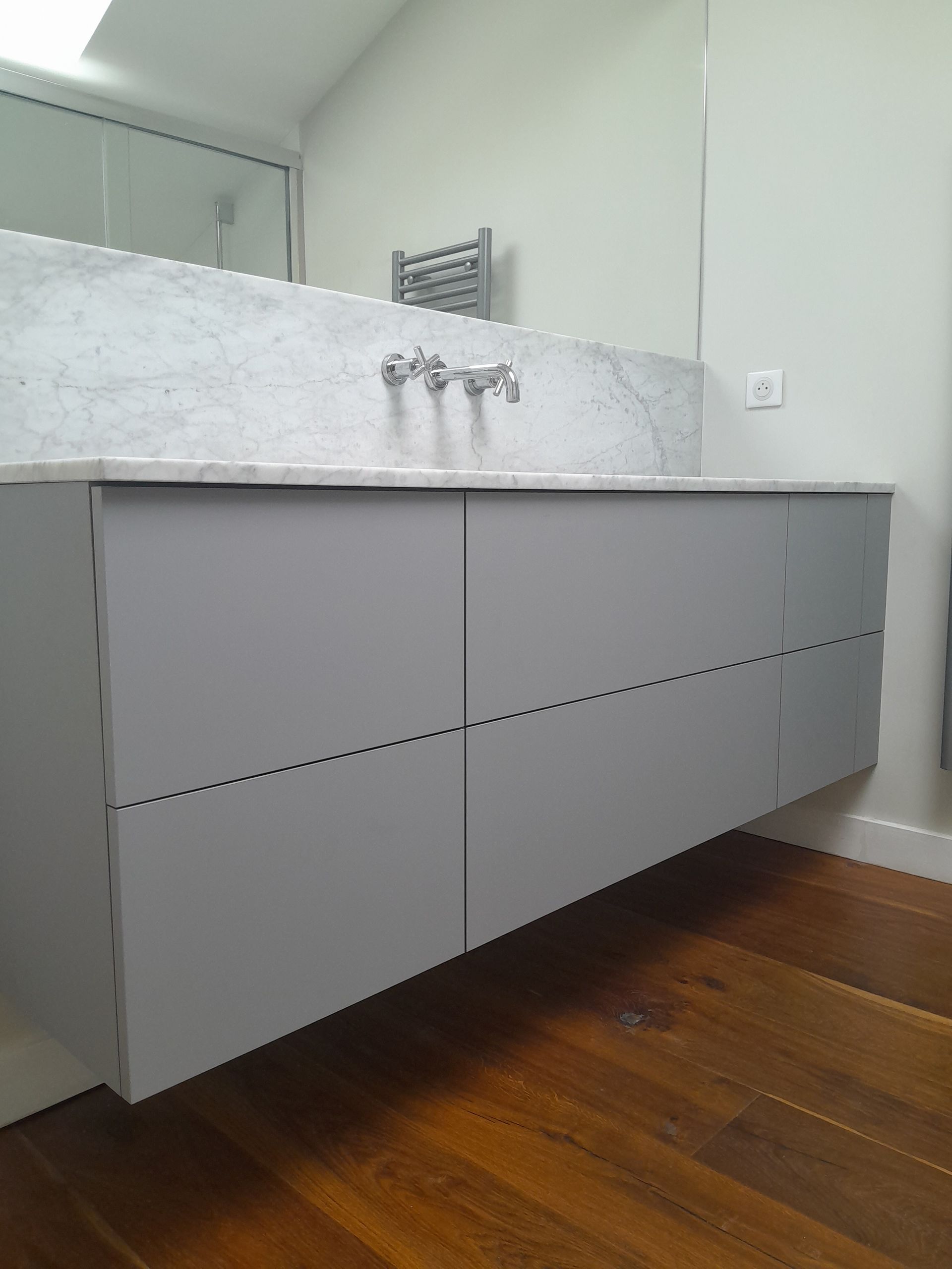 Meuble-lavabo de salle de bains avec flottant gris, dosseret en marbre et plancher en bois.