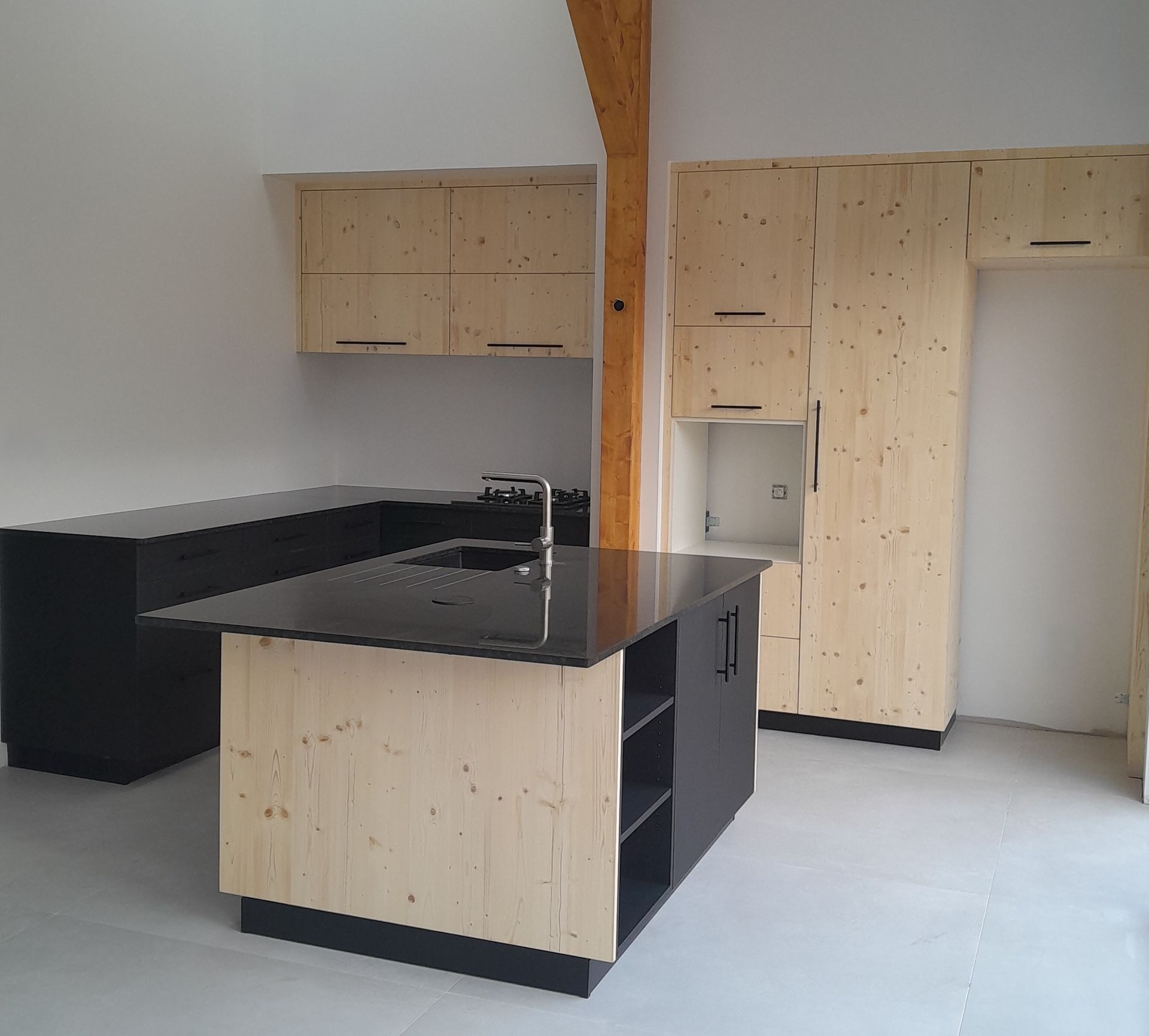 Cuisine moderne avec armoires en bois clair, comptoirs noirs et îlot central.