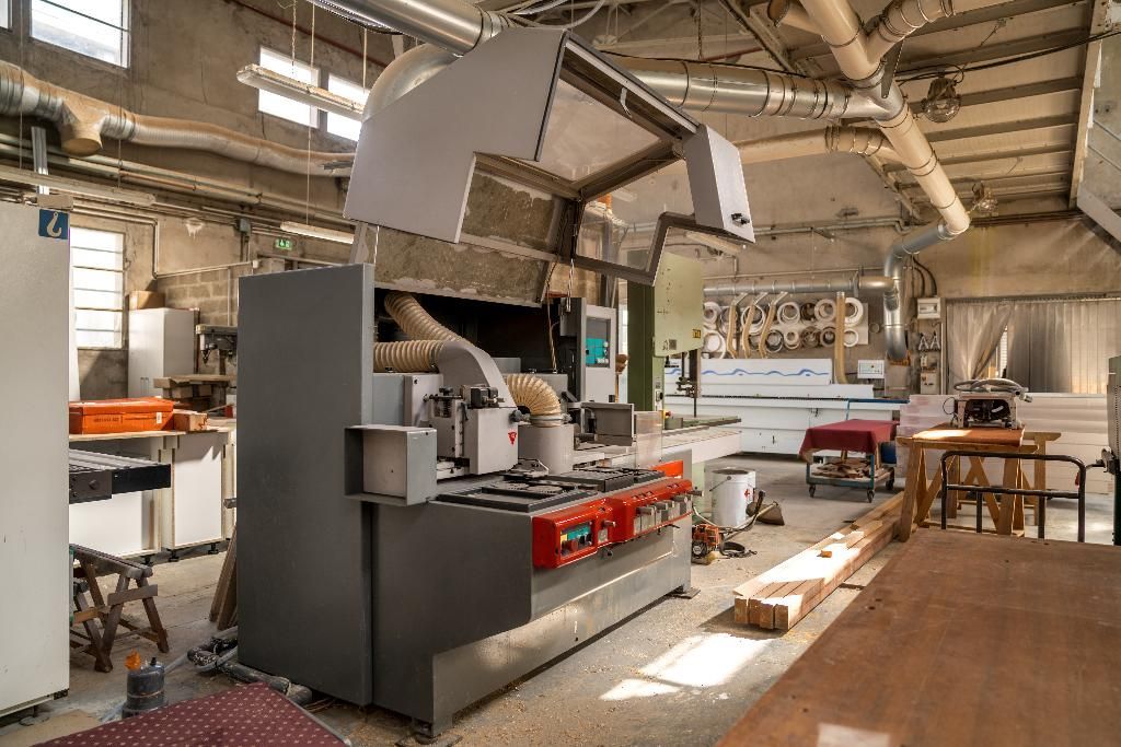 Atelier avec de grandes machines grises, des tuyaux apparents et divers établis.