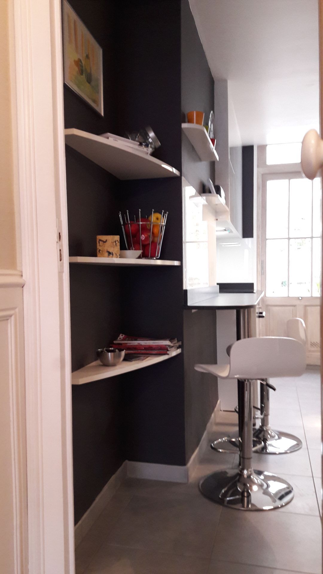 Étagères d'angle avec objets, tabourets de bar au comptoir et porte. Couleurs gris foncé et blanc.