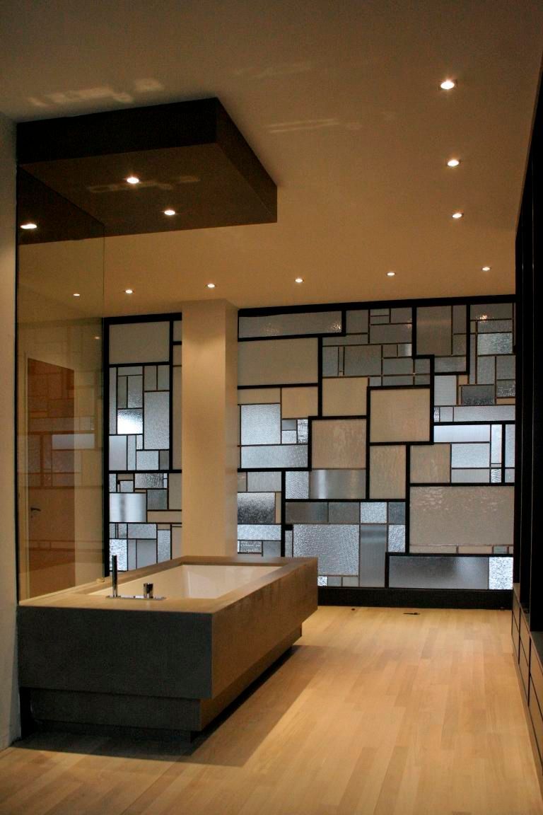Salle de bains moderne avec baignoire en pierre, mur en verre dépoli géométrique et plancher en bois.