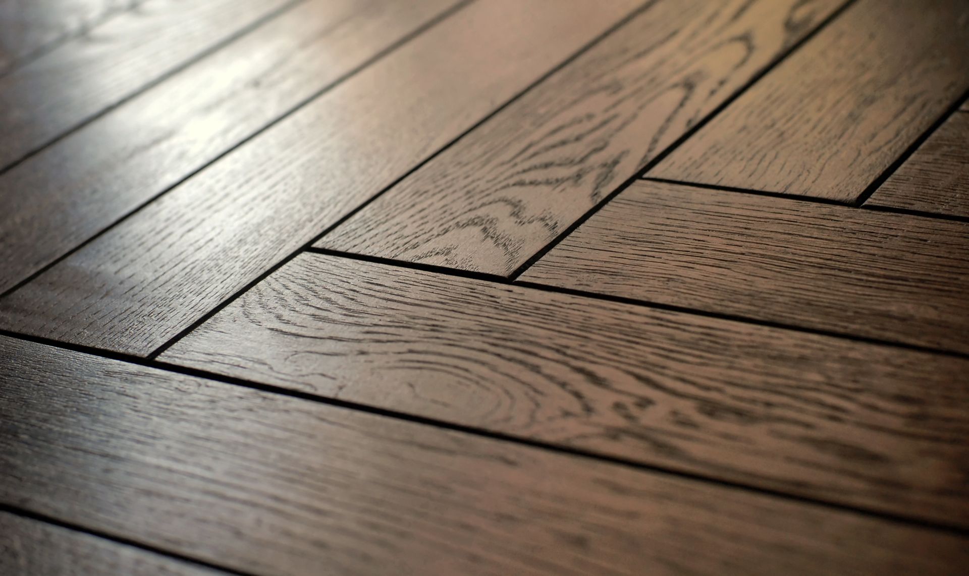 Gros plan d'un parquet en bois dur à motif à chevrons avec une teinture brun foncé.