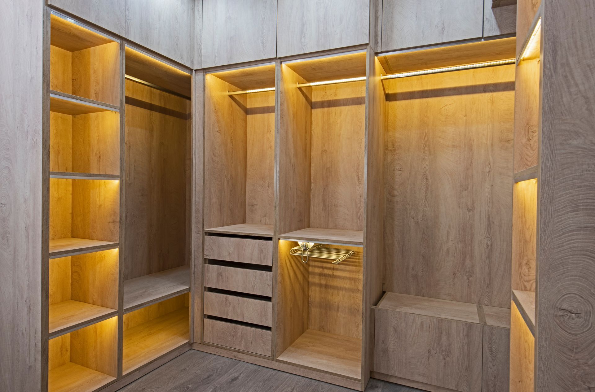 Dressing en bois avec étagères, tiroirs et tringles à vêtements ; éclairé par un éclairage chaleureux.