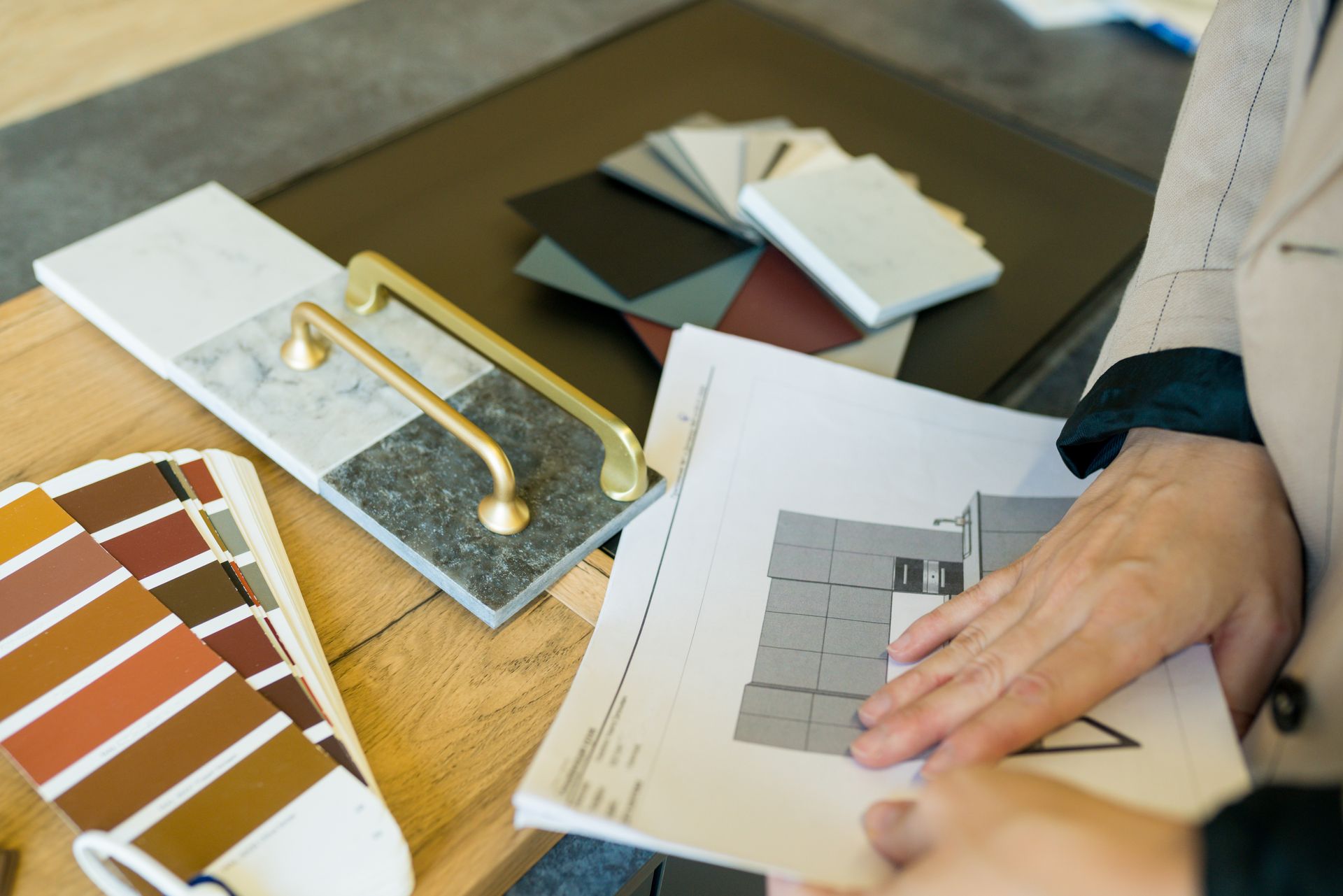 Personne tenant des plans architecturaux à côté d'échantillons de matériaux et de quincaillerie.