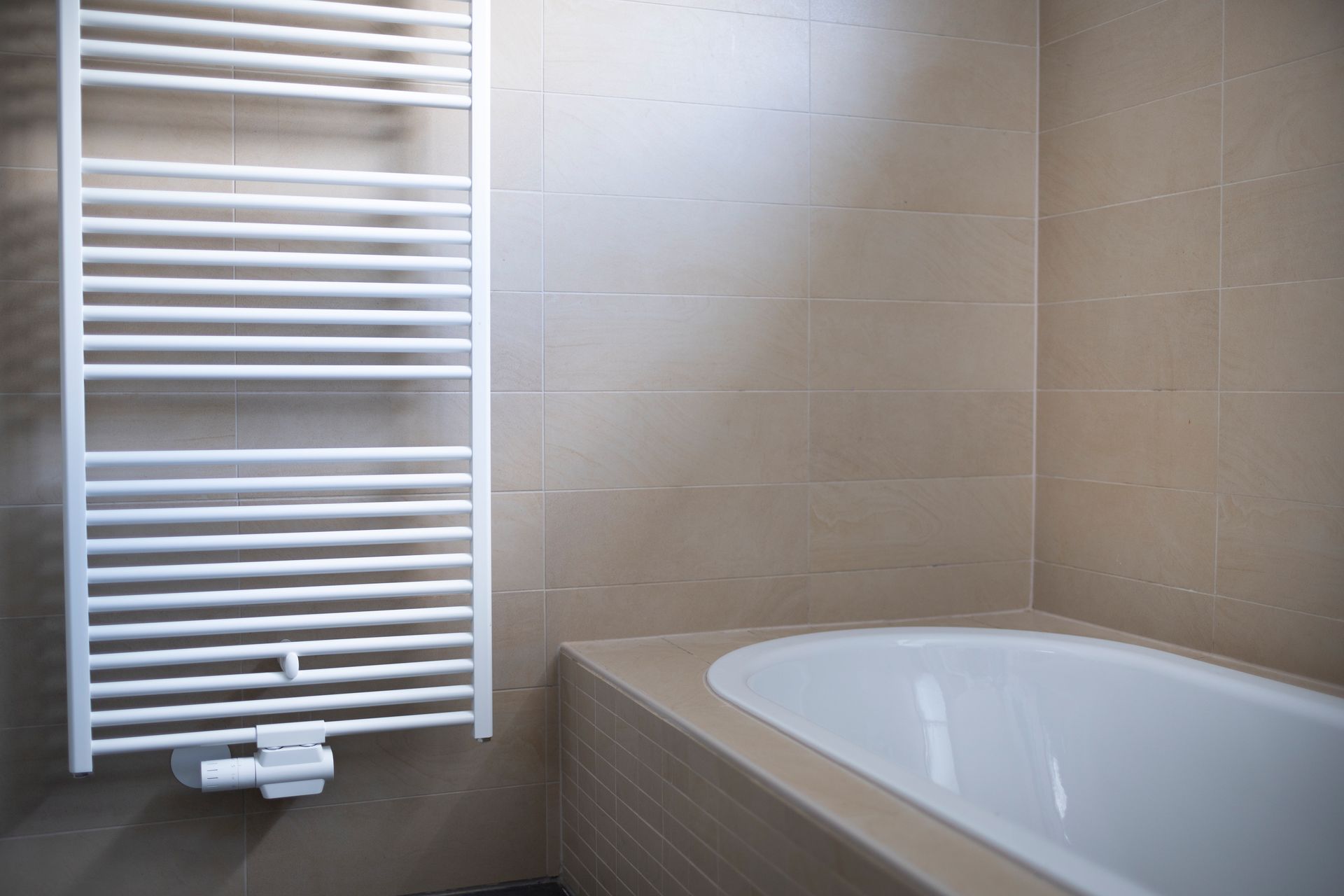 Radiateur sèche-serviettes blanc à côté d'une baignoire blanche dans une salle de bains carrelée.
