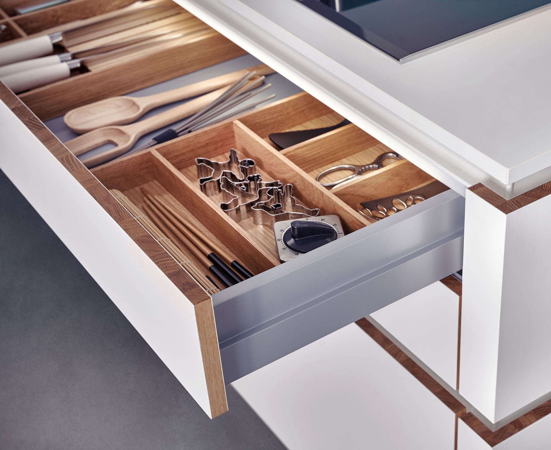 Tiroir de cuisine ouvert avec rangements en bois pour ustensiles. Armoires blanches avec intérieur gris.