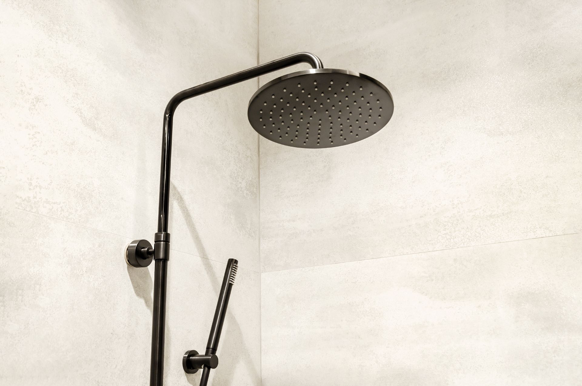 Pommeau de douche noir et douche à main contre un mur texturé gris clair.