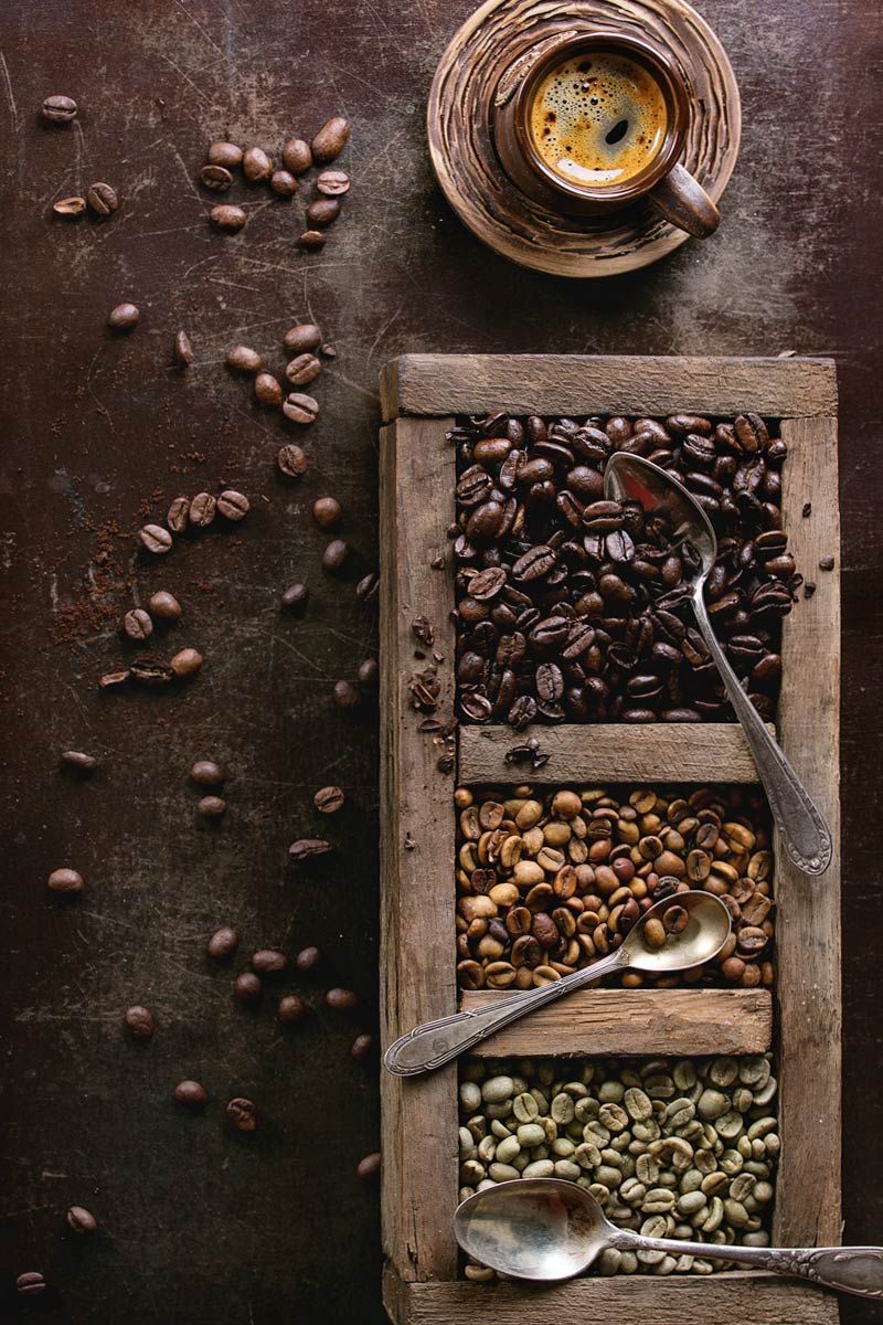 Una caja de madera llena de diferentes tipos de granos de café y una taza de café.