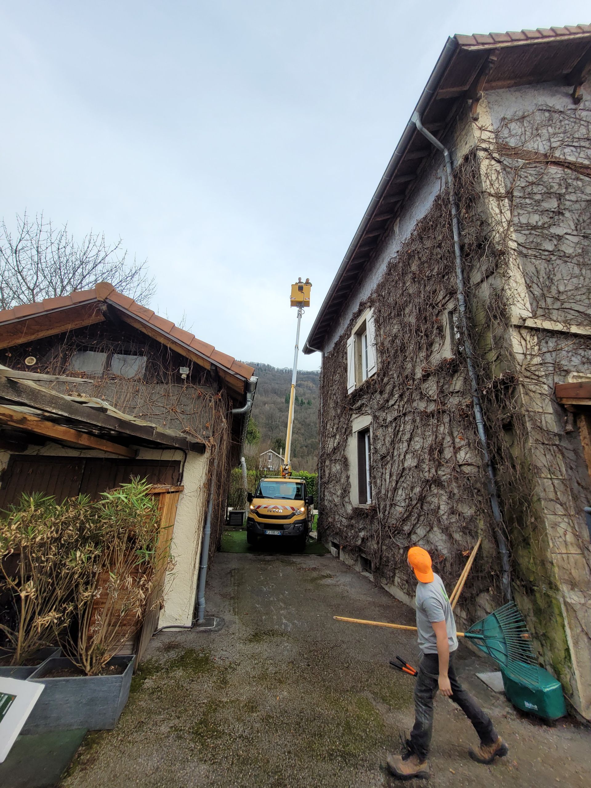 Ruelle de village étroite entre des maisons en pierre, avec une personne portant un casque orange près d'un véhicule stationné.