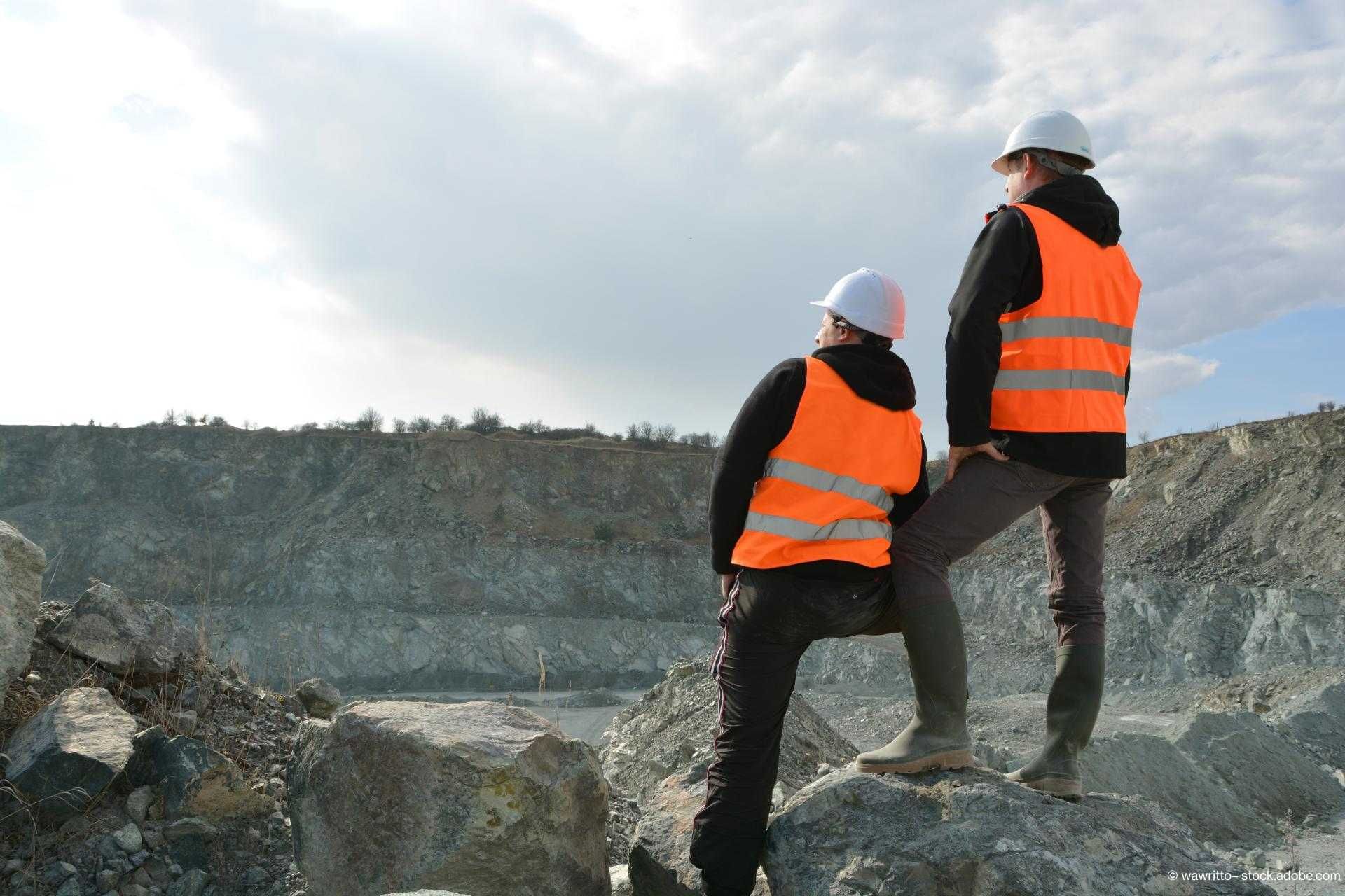 Zwei Bauarbeiter in oranger Weste stehen auf einem Hügel