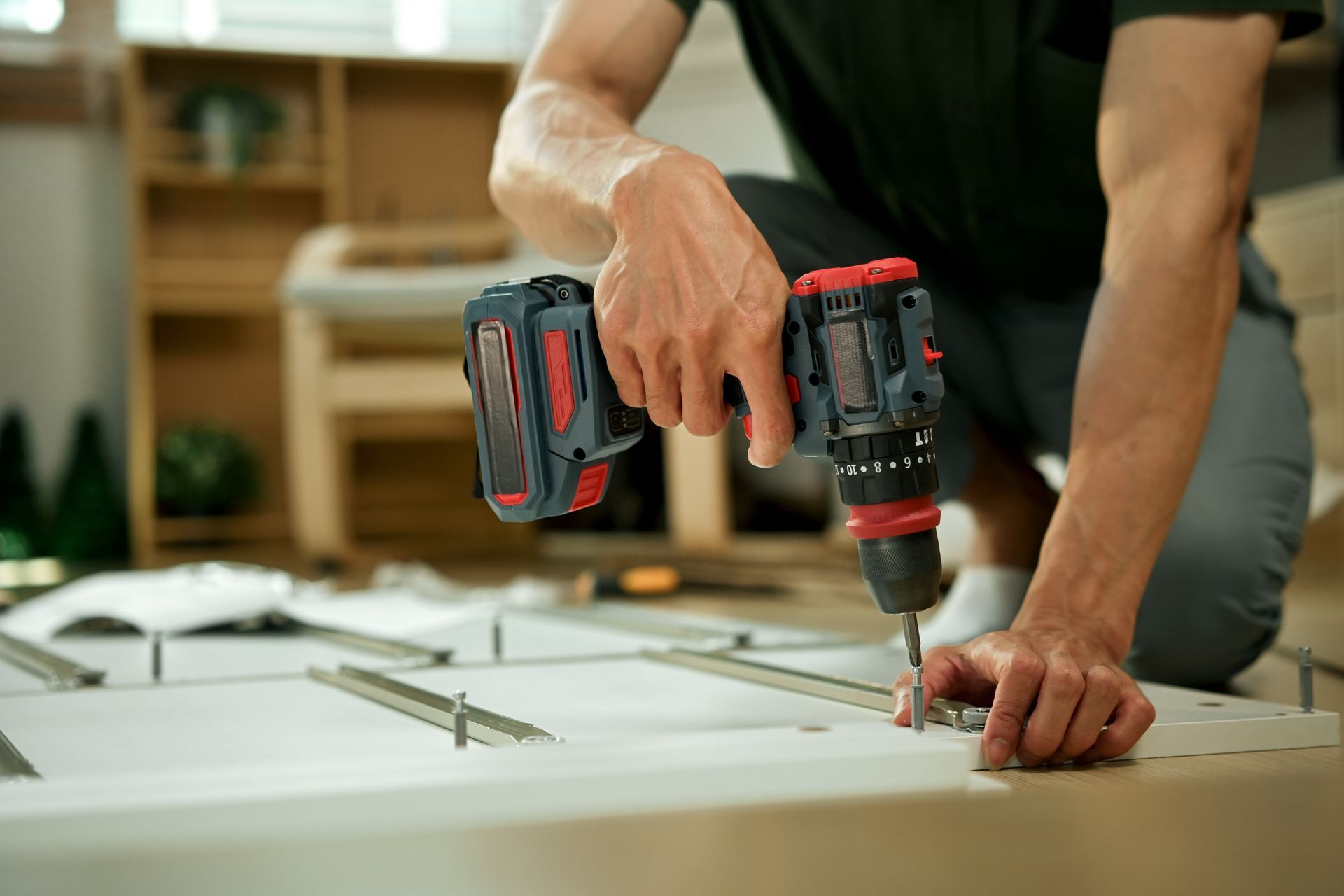 Une personne utilise une perceuse sans fil pour fixer une vis dans un panneau de meuble blanc en kit.