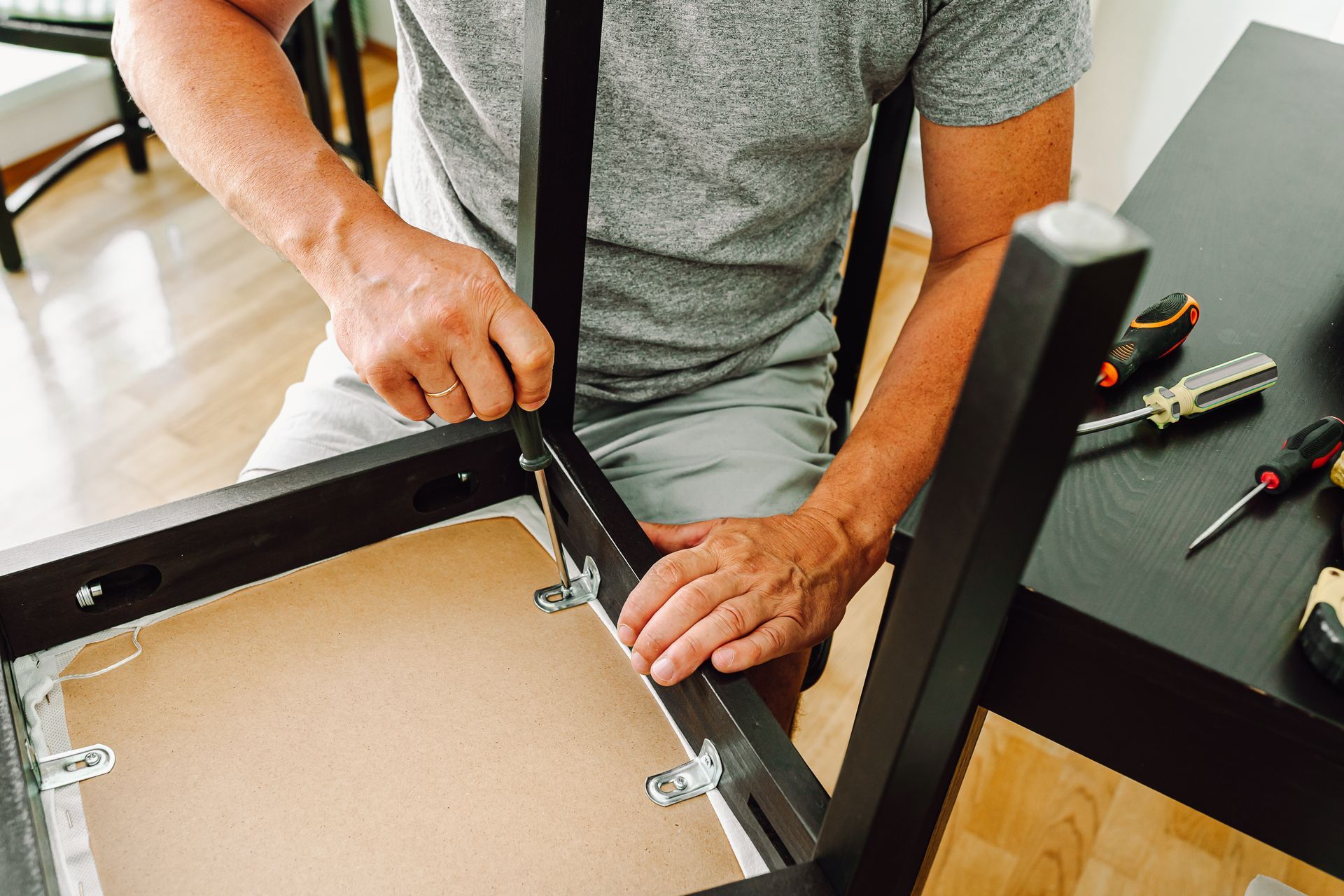 Une personne utilise un tournevis pour fixer un pied au cadre d'une chaise noire.