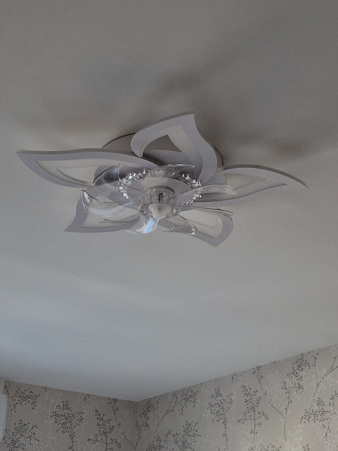 Un plafonnier LED moderne, blanc, en forme de fleur, avec un centre translucide semblable à du cristal, monté sur un plafond blanc.