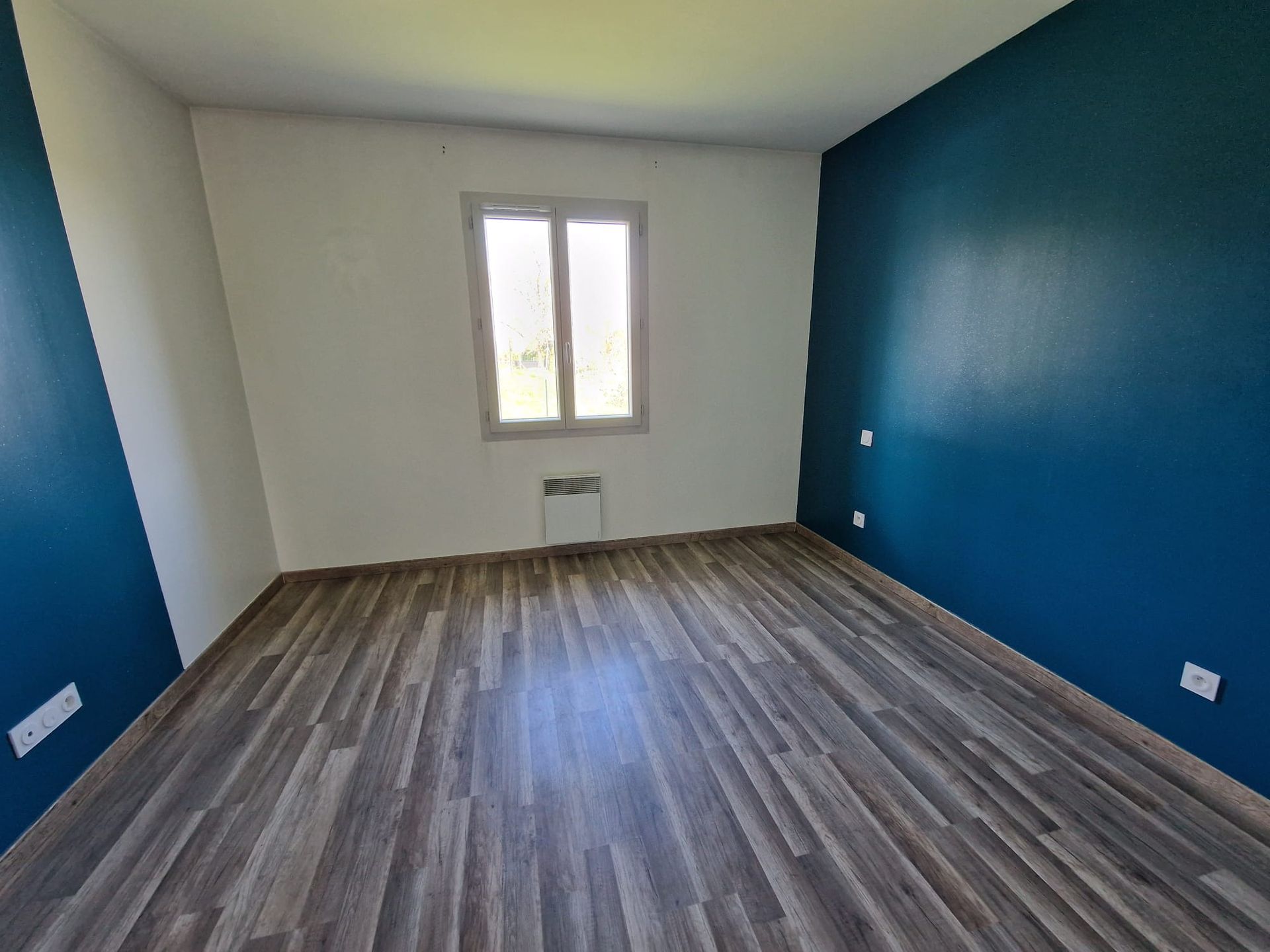 Une pièce vide avec un sol en parquet, des murs blancs et un grand mur bleu sur la droite.