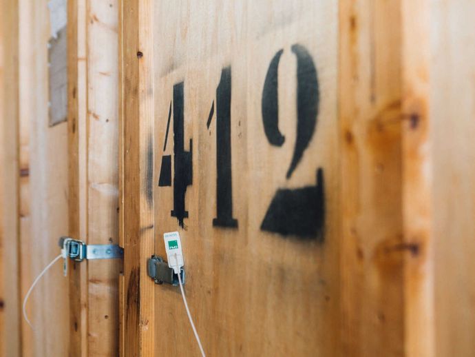 Porte d'unité de stockage en bois avec le numéro 412 peint au pochoir en noir et un câble blanc fixé à la porte.