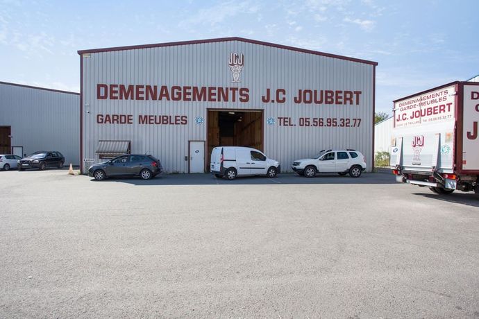 Extérieur de l'entrepôt de la société de déménagement JC Joubert avec des véhicules stationnés.