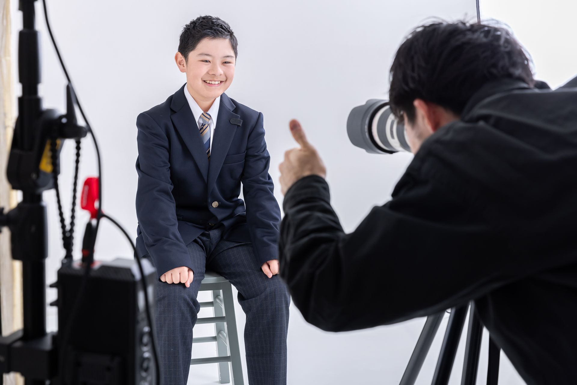 Un garçon souriant habillé dans un uniforme scolaire, qui se fait prendre en photo par un photographe.