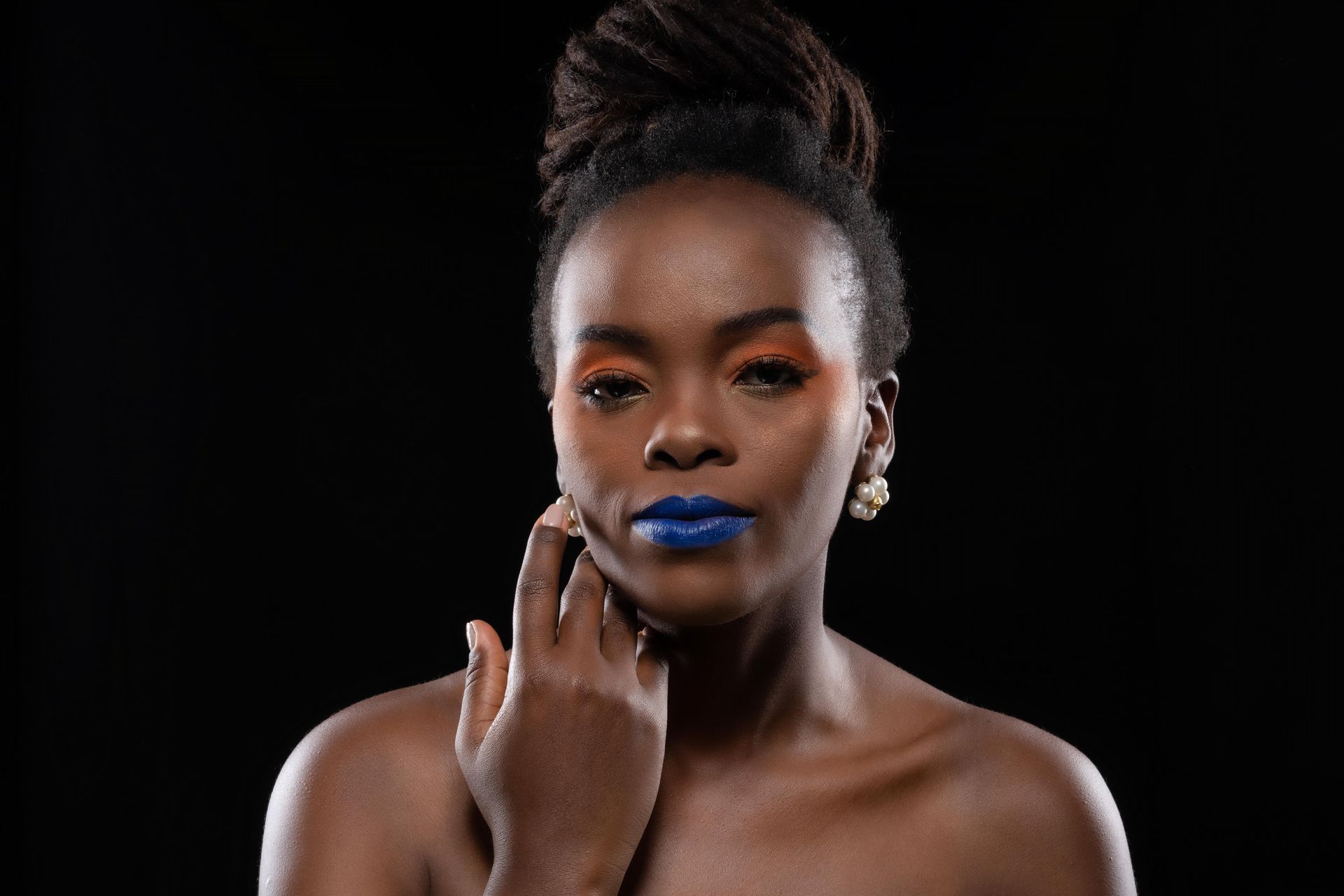 Portrait sur fond noir d'une femme maquillée, posant une main sur son visage.