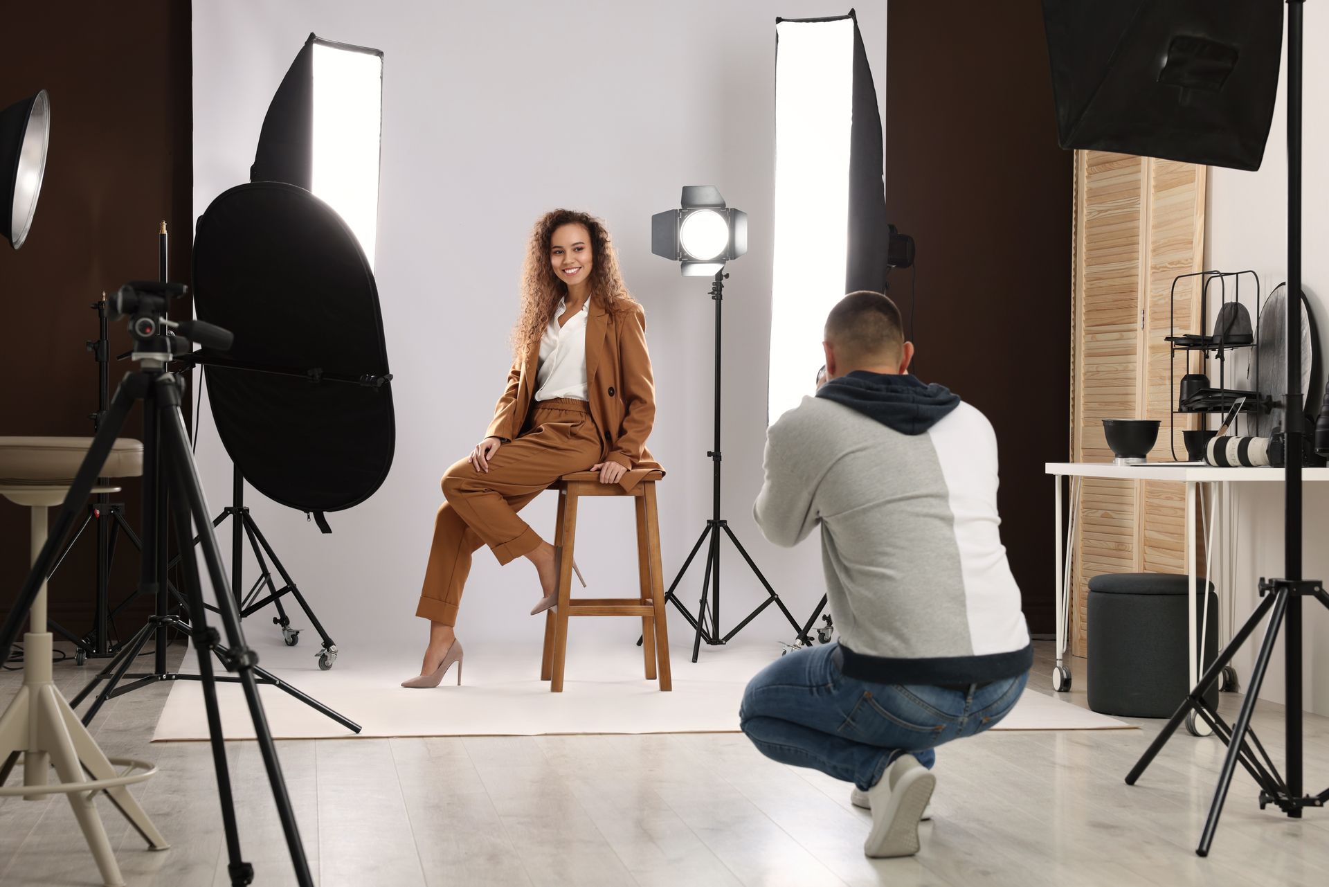 Une femme pose sur un tabouret avec un photographe qui la prend en photo dans un studio.