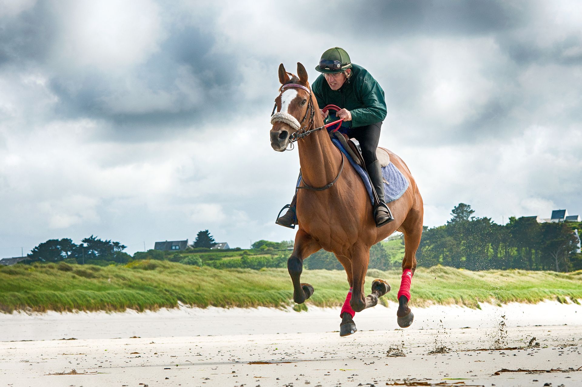 Un cavalier et son cheval galopant sur une plage de sable sous un ciel nuageux.