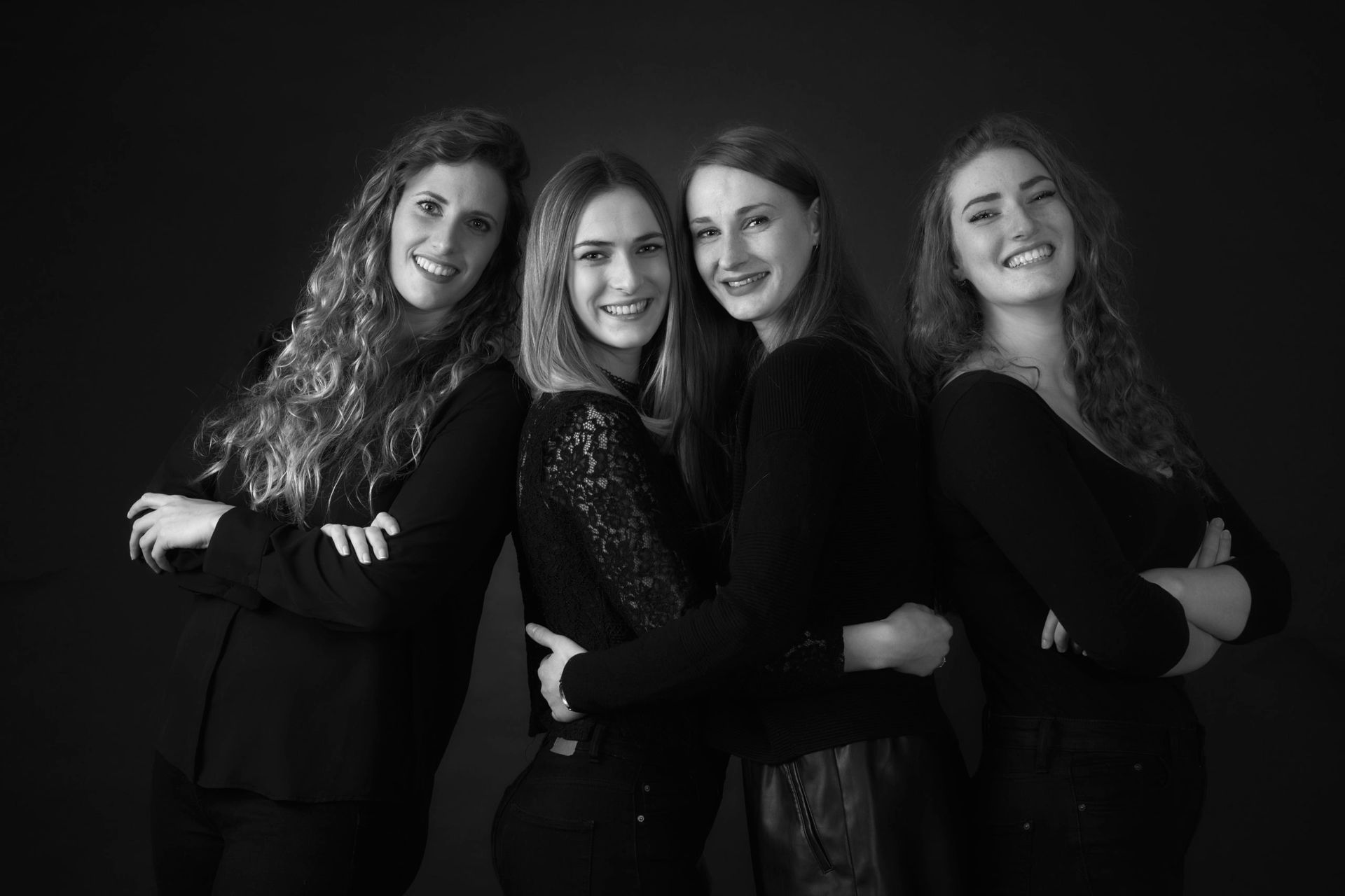 Quatre femmes souriantes, les bras croisés, posent ensemble sur un fond sombre.