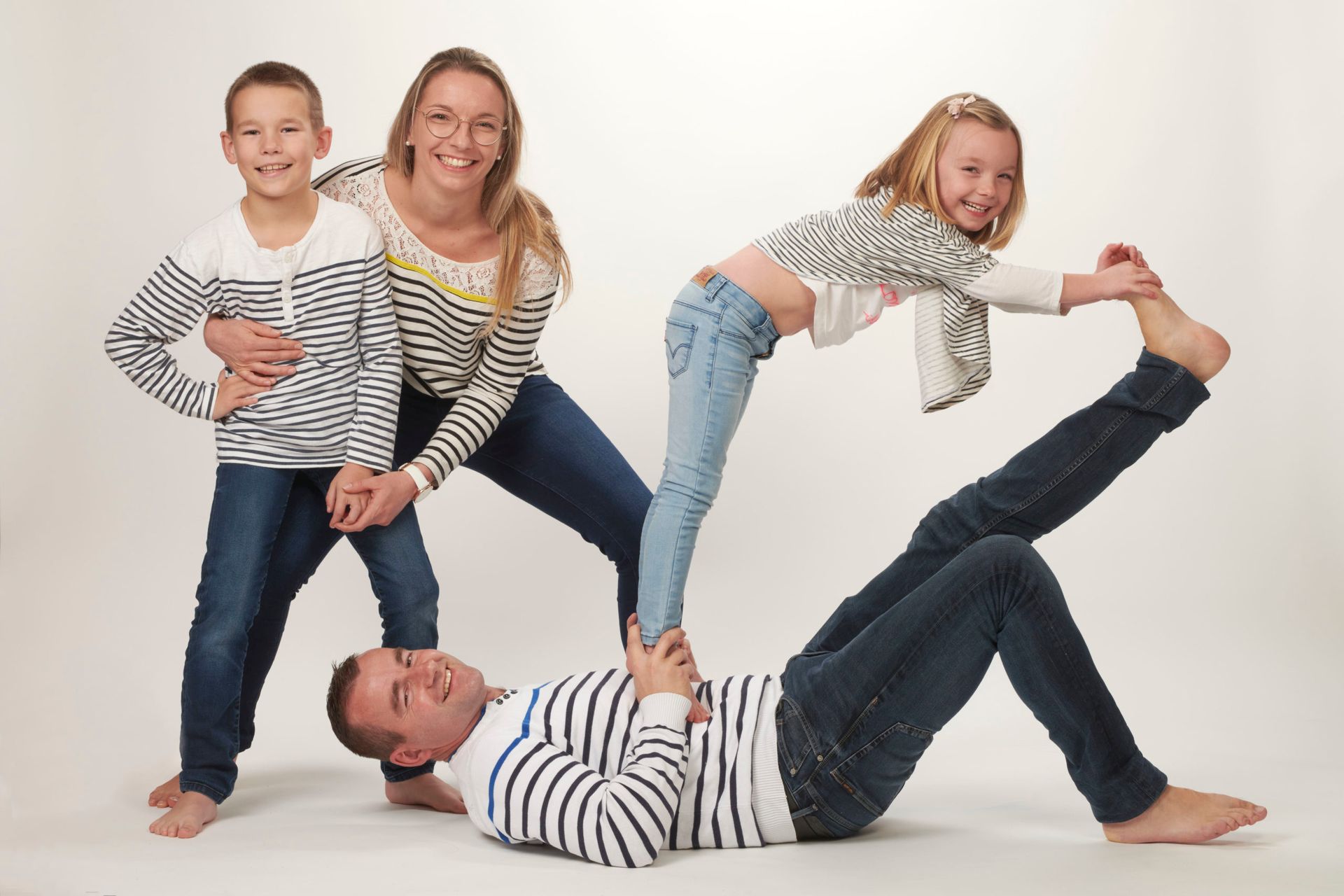 Une famille en tenue décontractée réalise une pose acrobatique sur fond blanc.