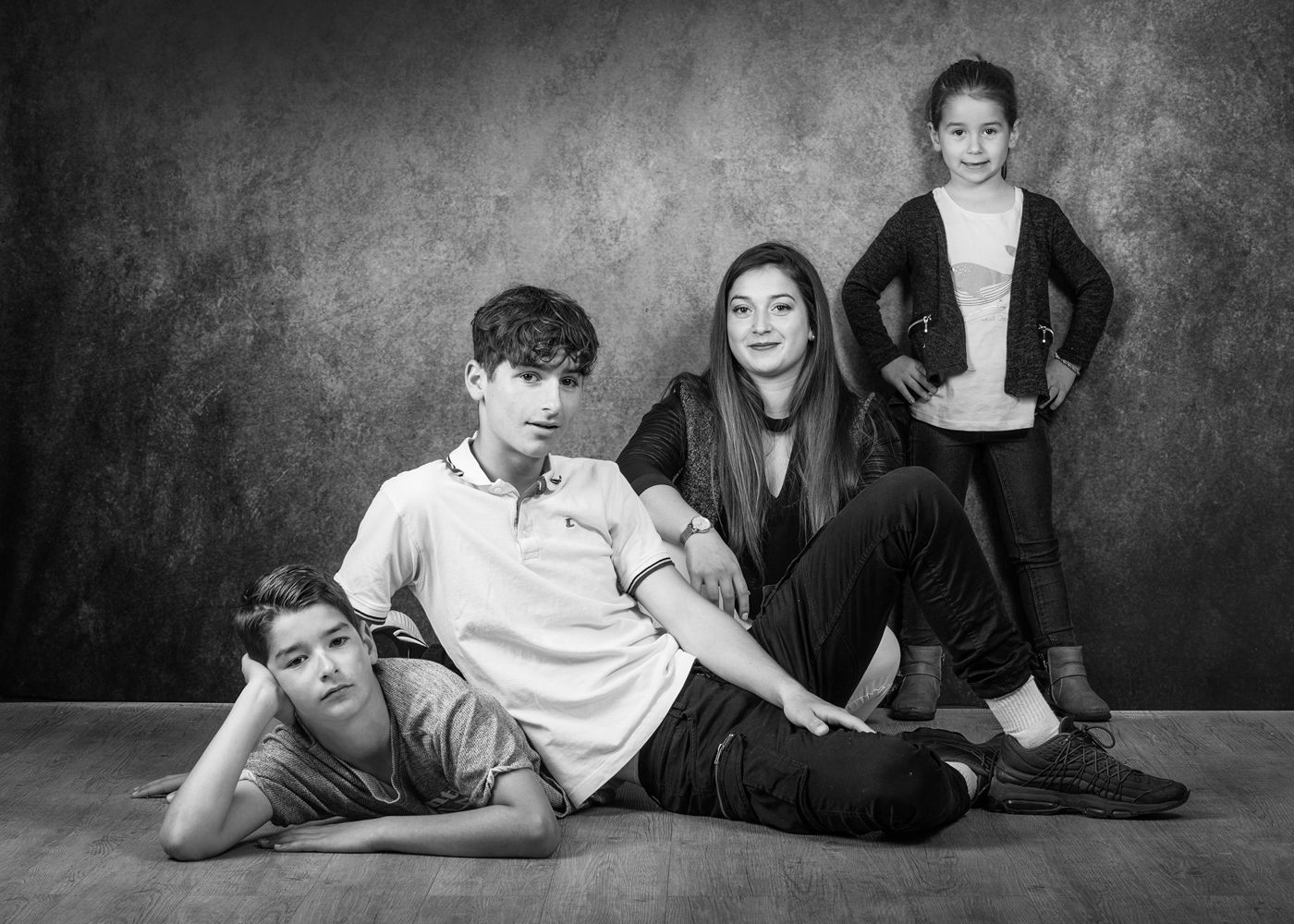 Portrait de famille où quatre frères et sœurs posent devant un fond gris texturé.