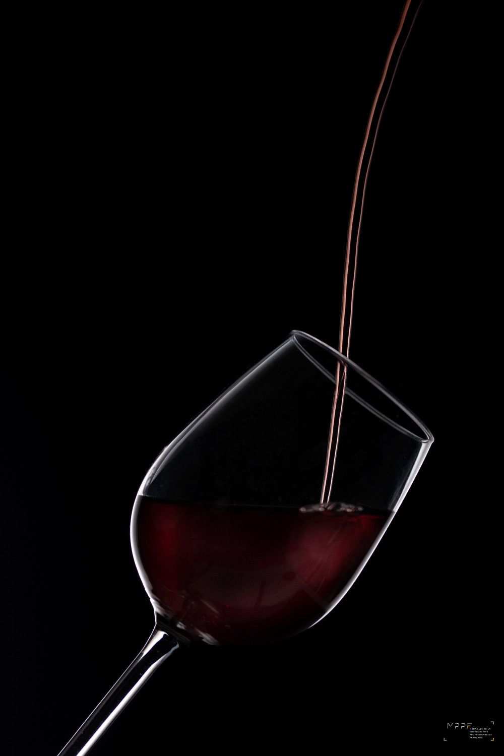 Du vin rouge versé dans un verre incliné sur fond noir.