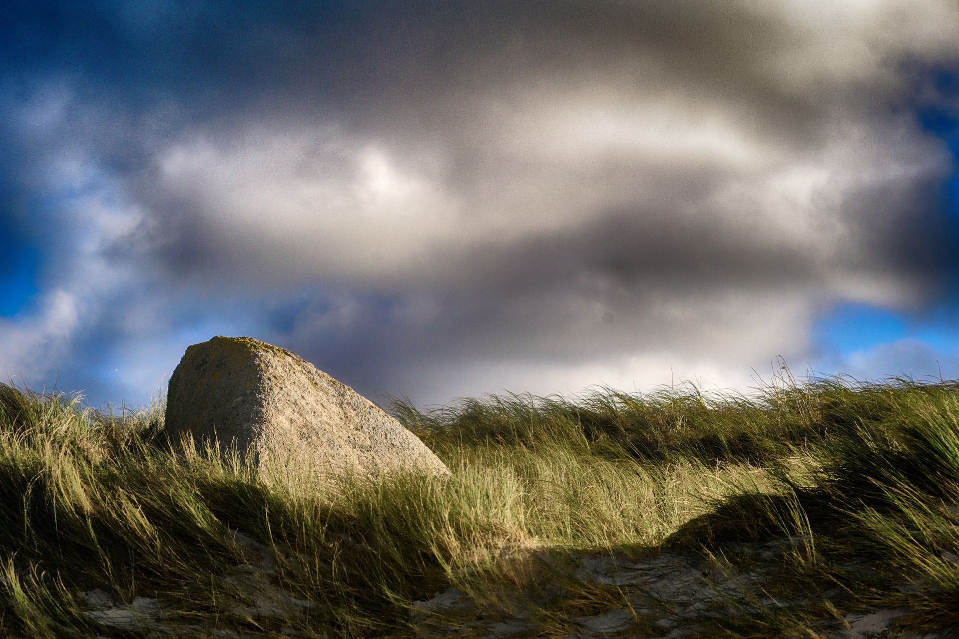 Un rocher dans une dune herbeuse.