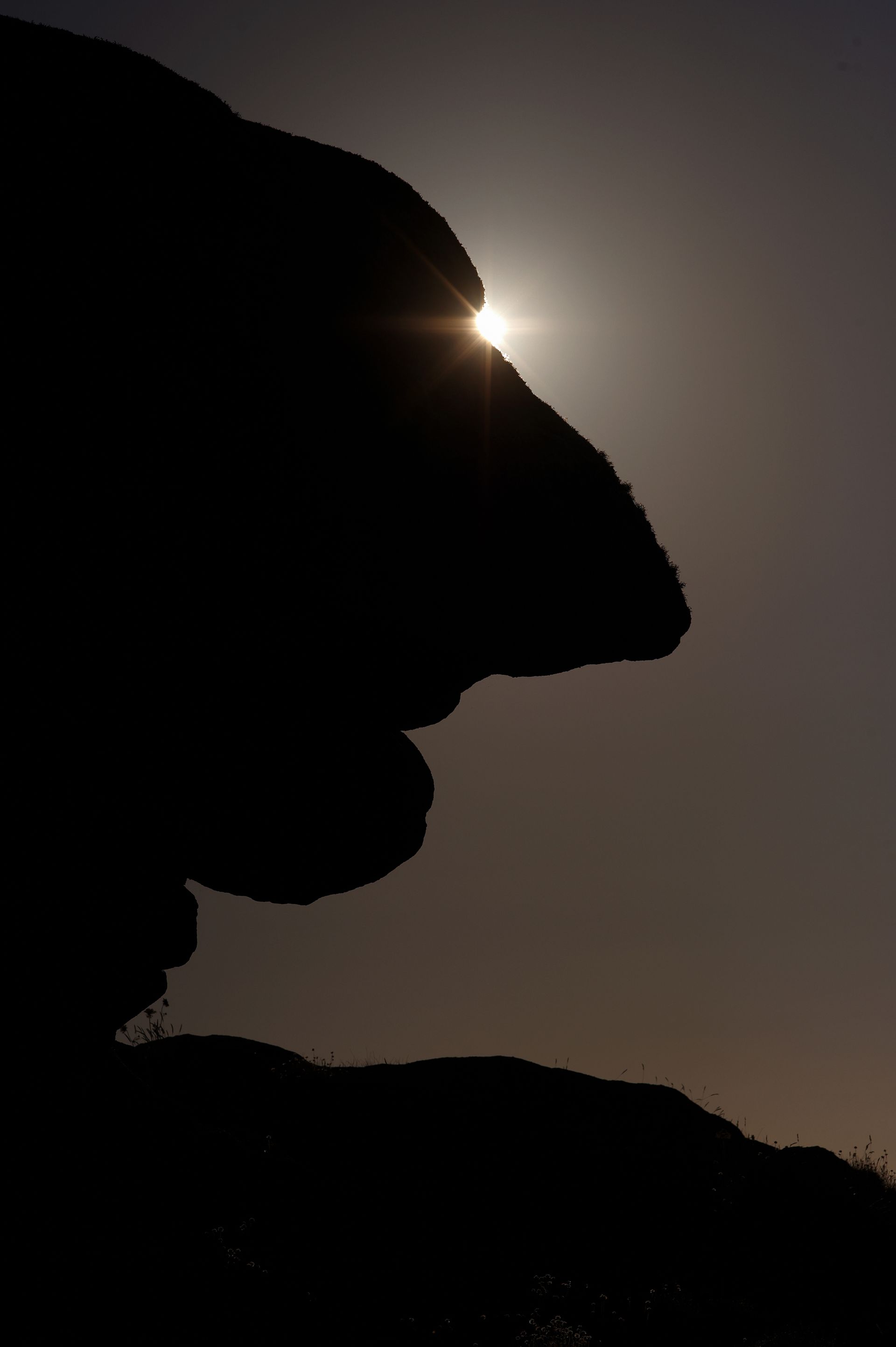 Silhouette d'une formation rocheuse se détachant sur un soleil éclatant, ressemblant à un visage de profil.