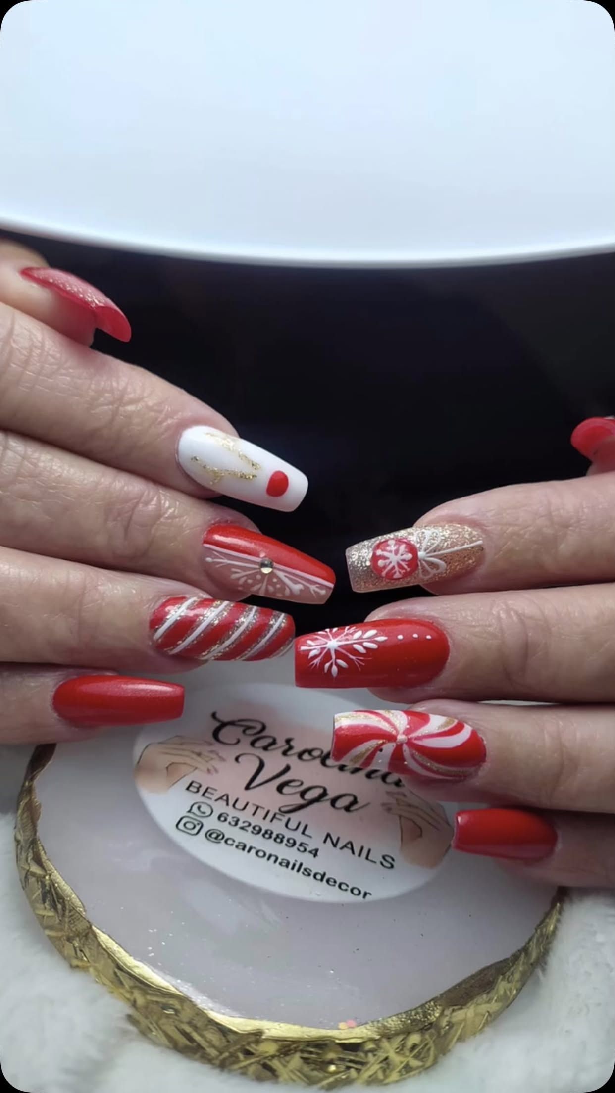 Las uñas de una mujer están pintadas de rojo y blanco con un diseño de bastón de caramelo.