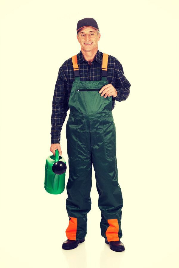 Un hombre con mono sostiene una regadera verde.