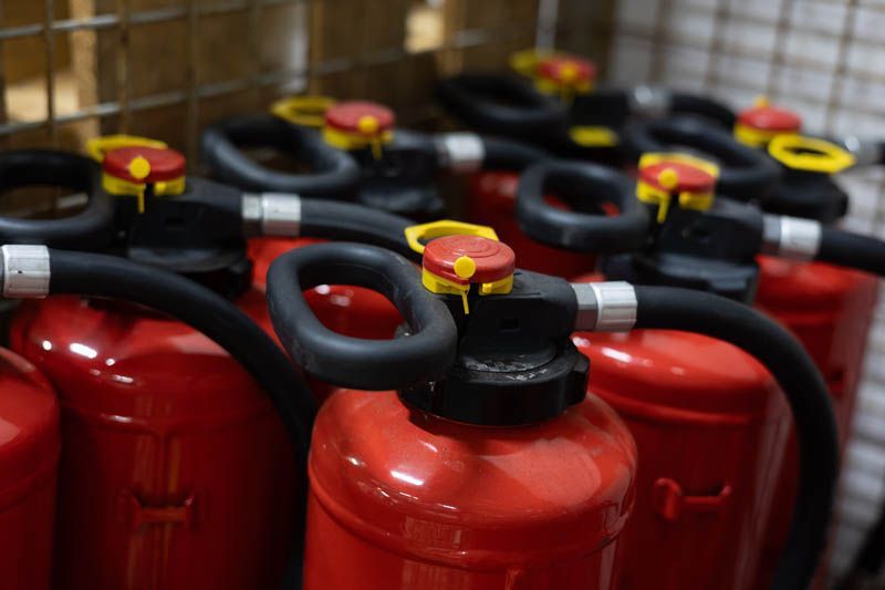 Rote Feuerlöscher mit schwarzen Schläuchen und Griffen.