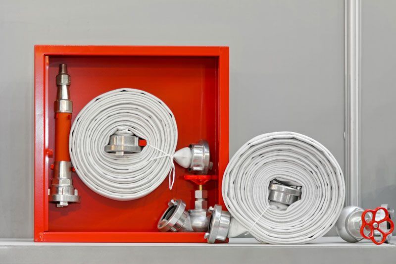 Roter Feuerwehrschlauchschrank mit Schlauch und Düse, grauer Hintergrund.