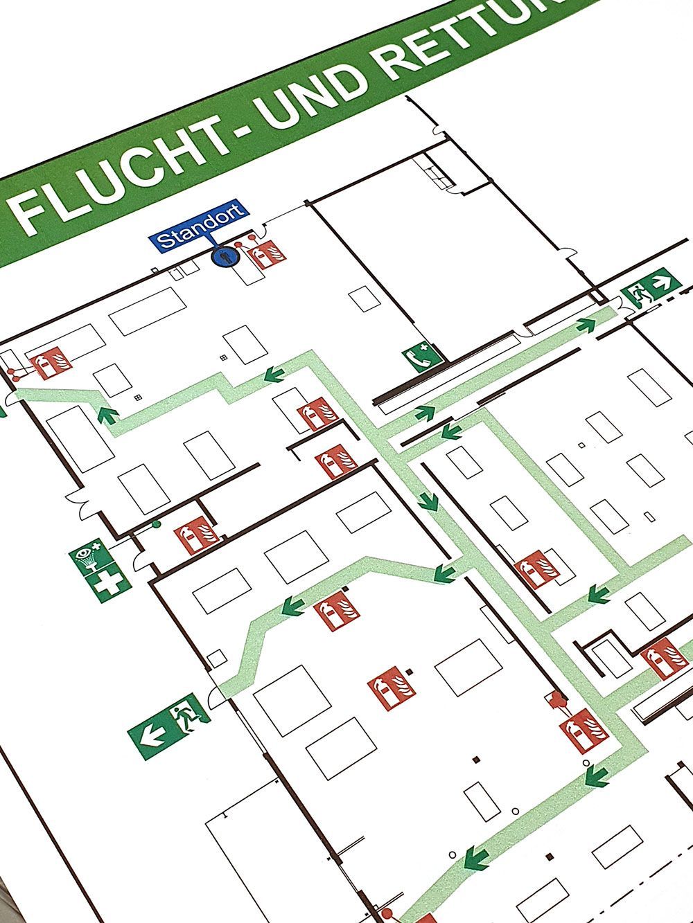 Notausgangsplan mit grünen Fluchtwegpfeilen und roten Feueralarmsymbolen.
